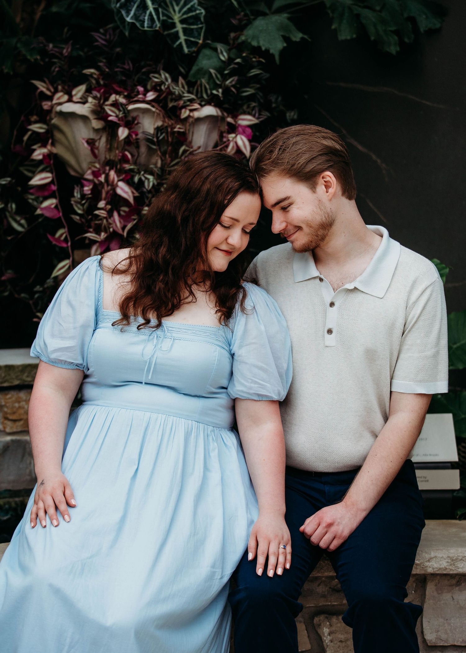 Couple sitting close together smiling softly, woman in blue dress, man in cream polo shirt.
