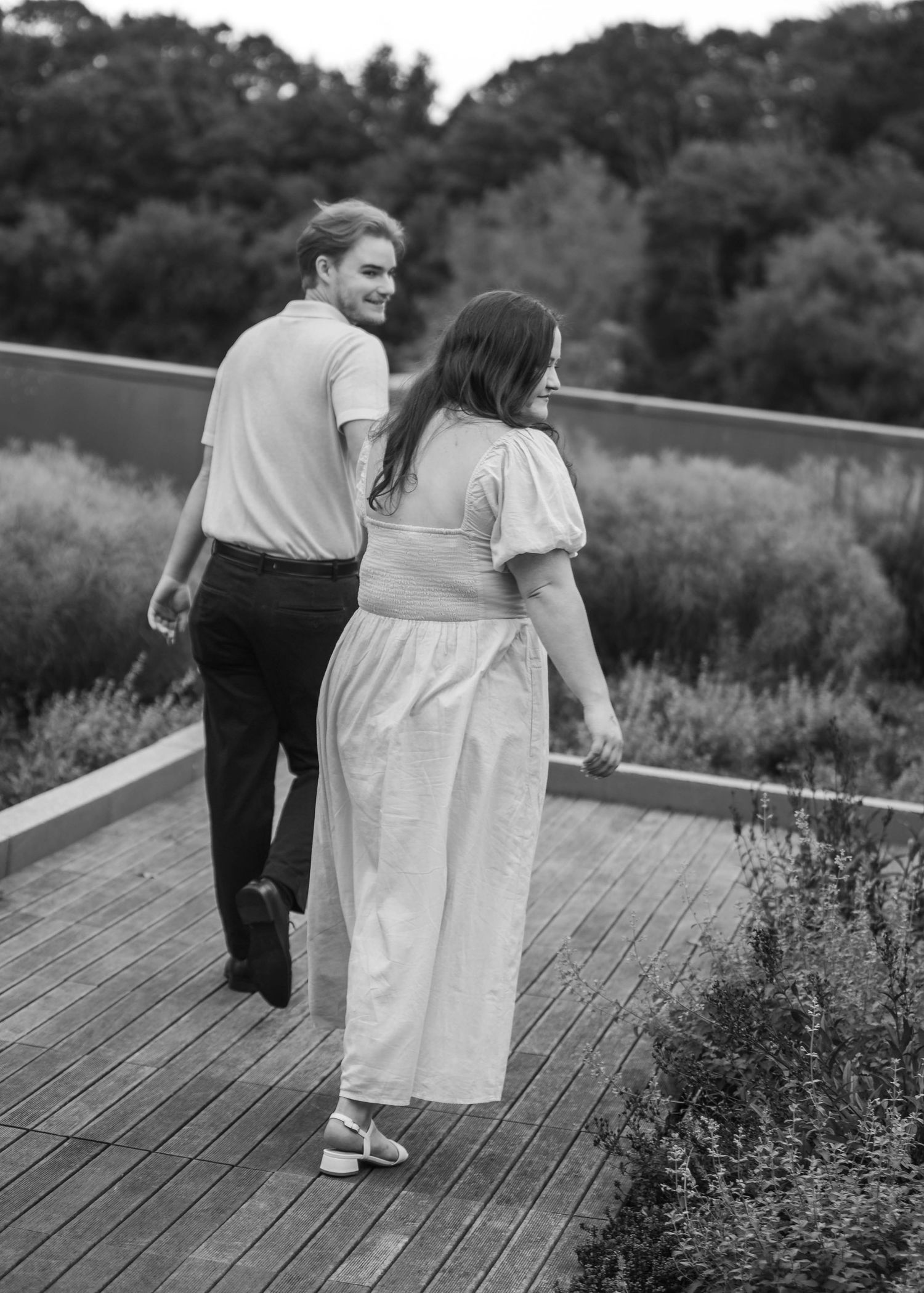 Black and white photo of couple walking hand in hand along a wooden deck with lavender.