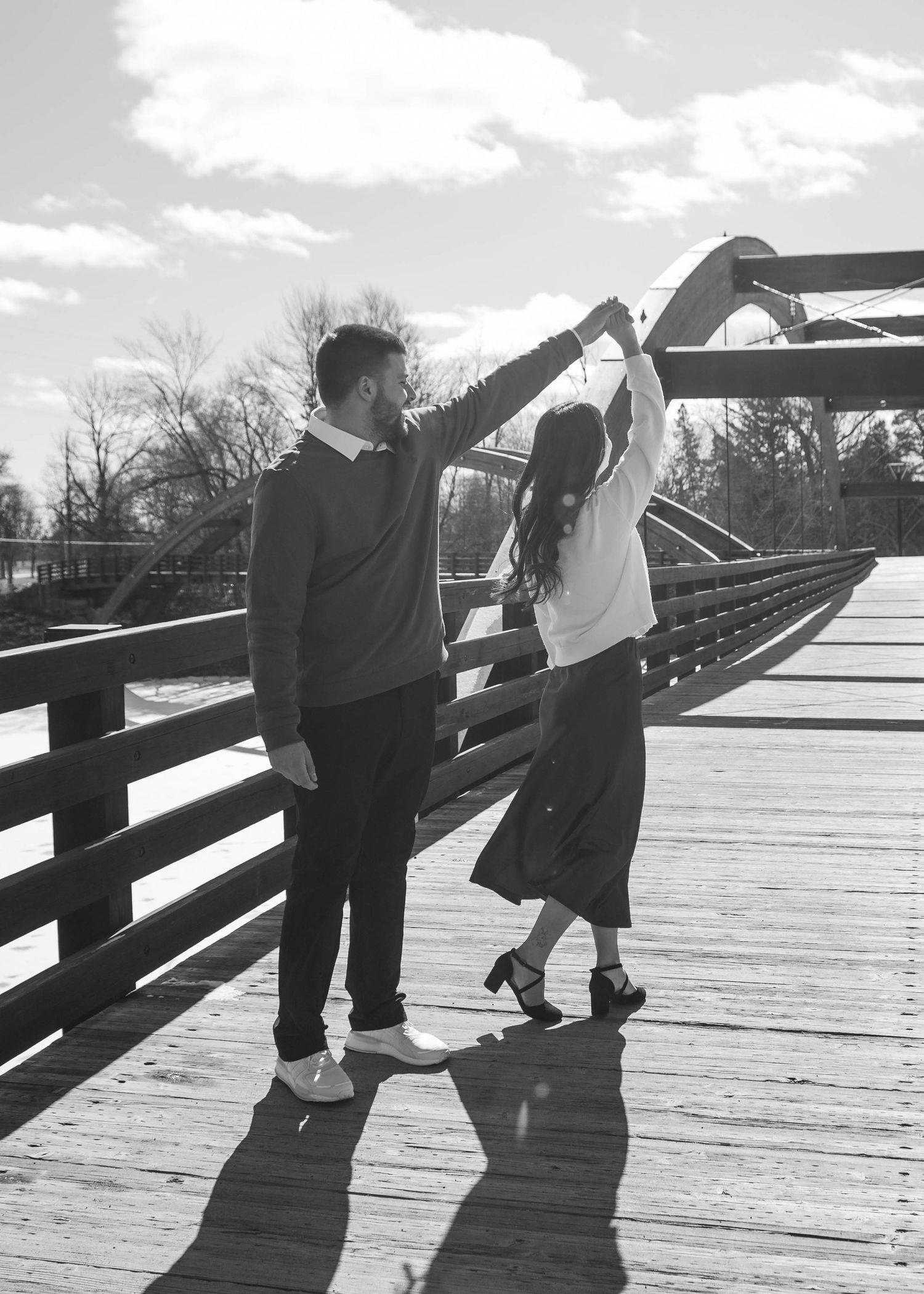 Black and white photo of couple dancing on a wooden bridge, man spinning woman under raised arms.