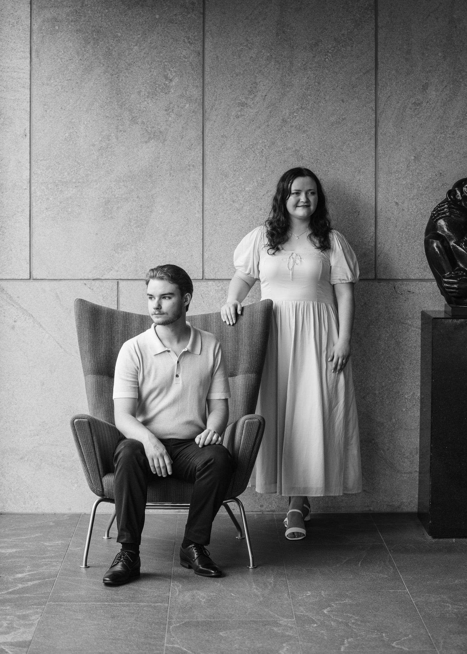 Black and white portrait of a couple posing elegantly indoors, man seated in a chair.