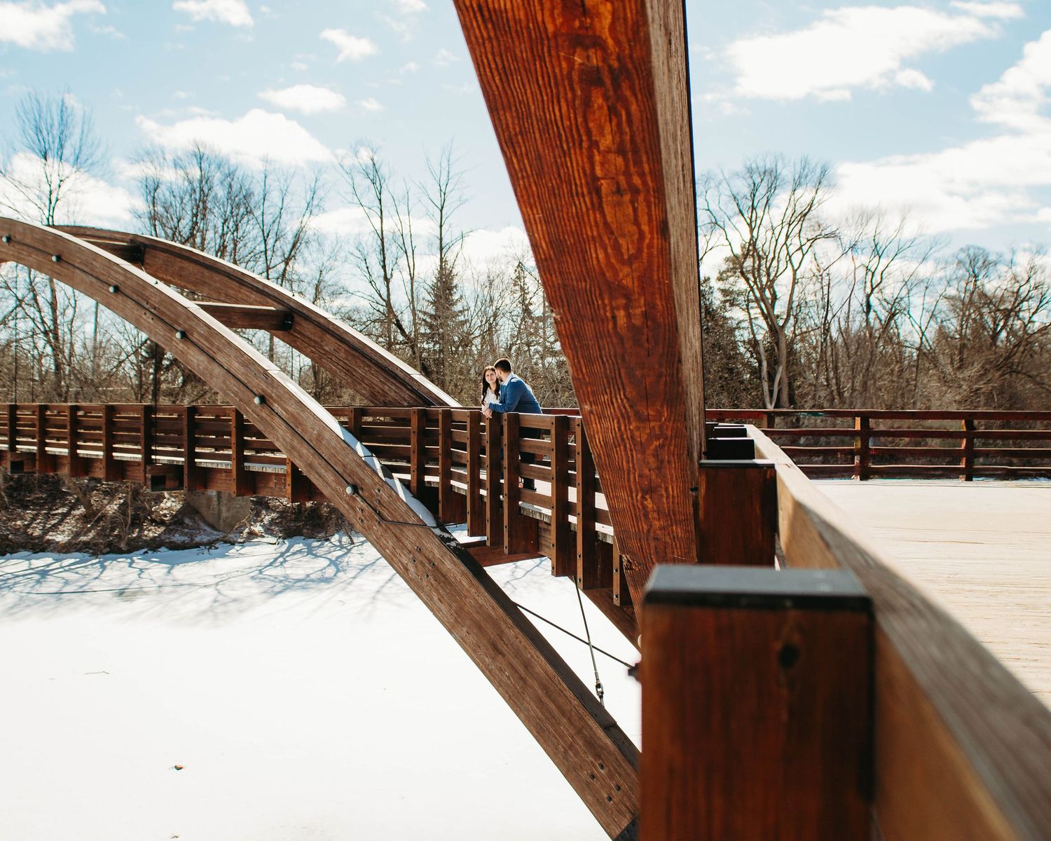 Couple sharing a romantic moment on a rustic wooden arched bridge surrounded by winter trees.