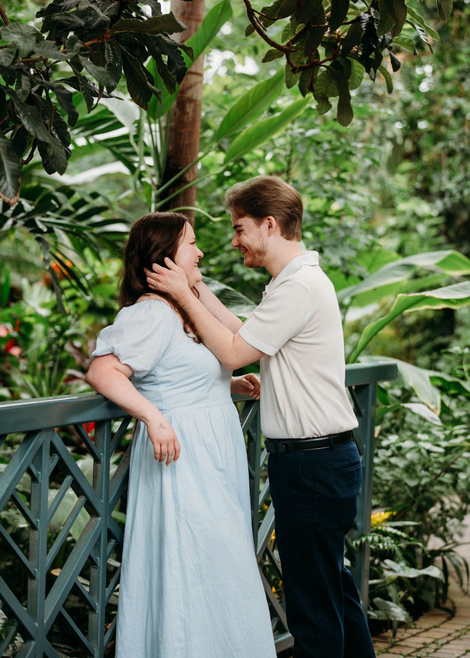 Couple sharing a tender moment on a bridge surrounded by tropical greenhouse plants.