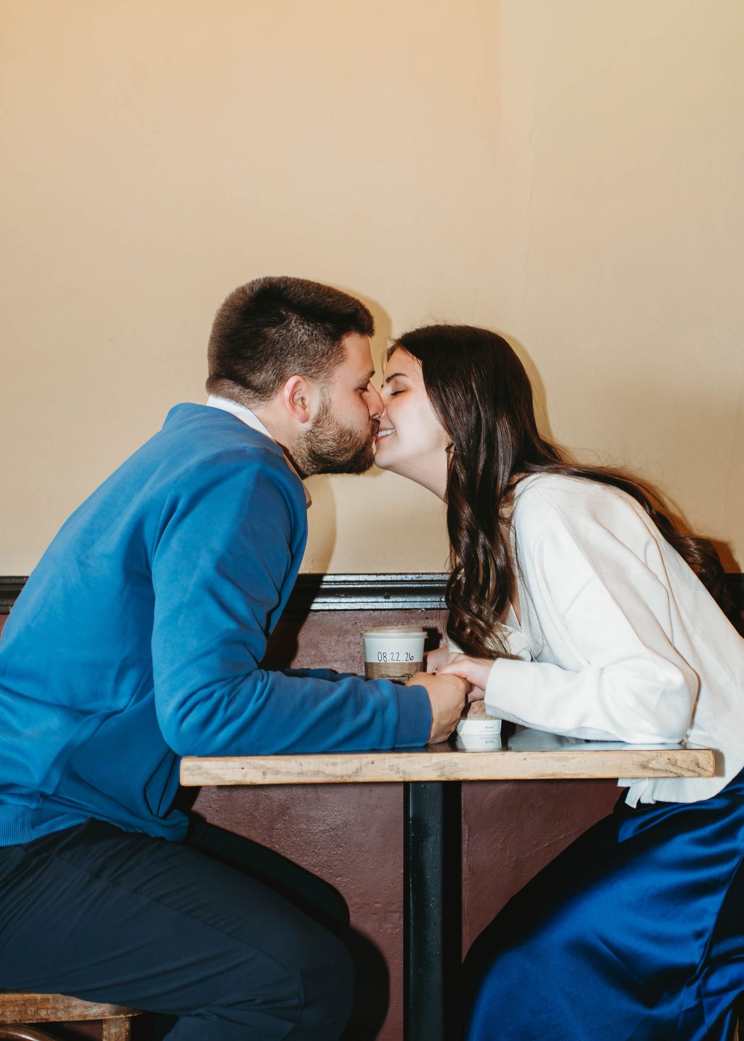 Engaged couple sharing a kiss across a small cafe table during their indoor engagement session.
