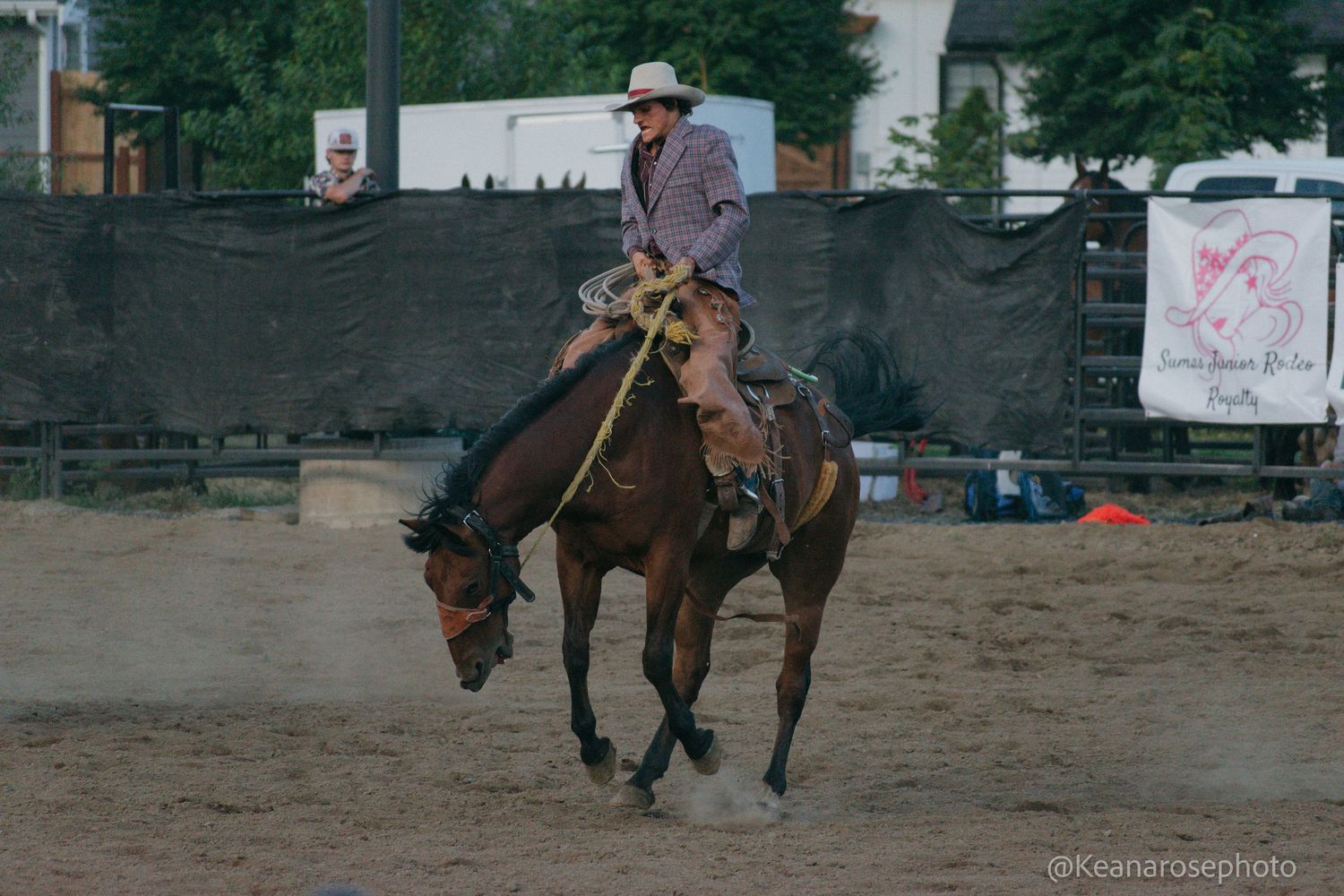A cowboy rides a brown horse across a dusty rodeo arena.