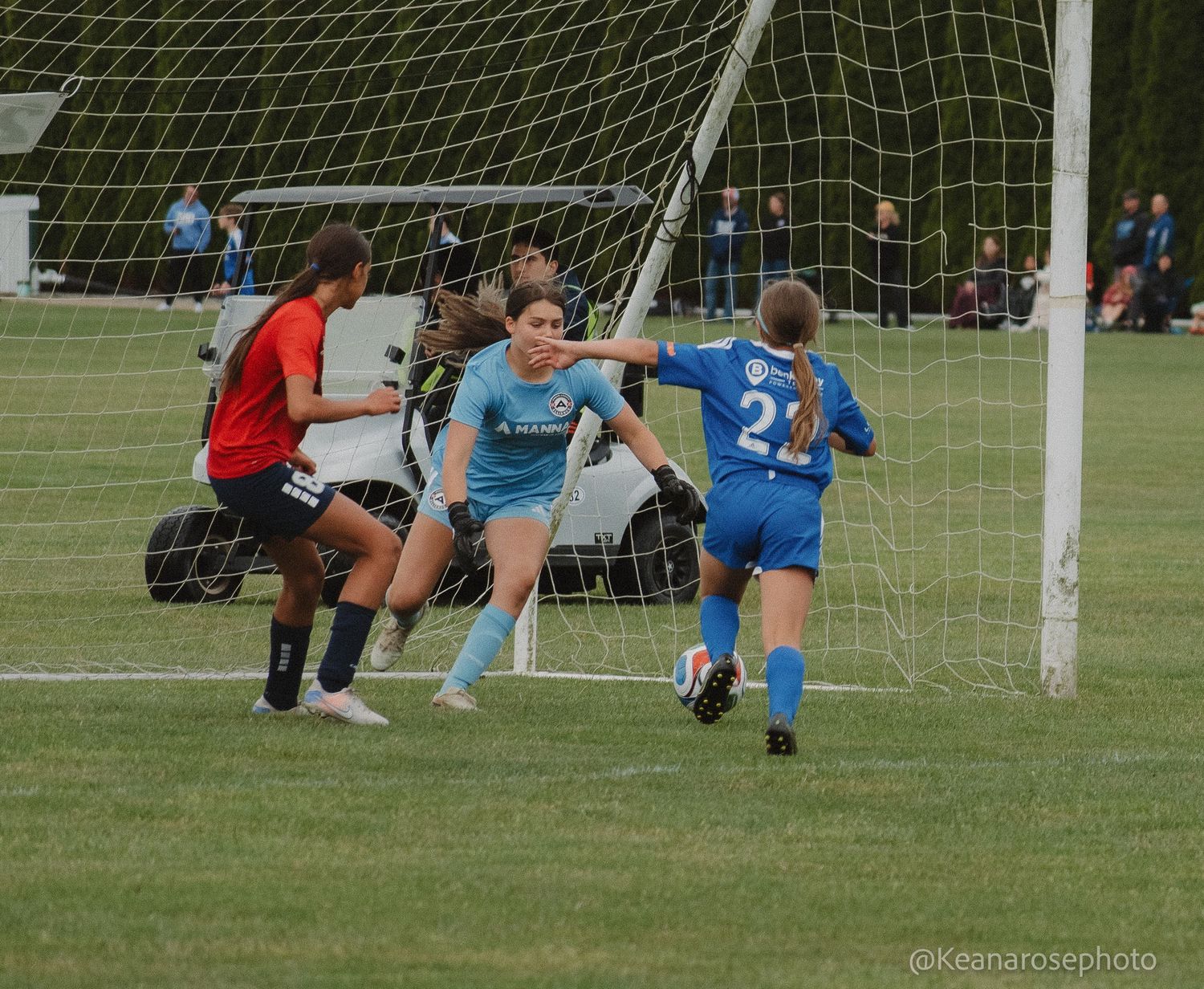 Female soccer goalkeeper in teal uniform defends goal during a competitive youth soccer match.