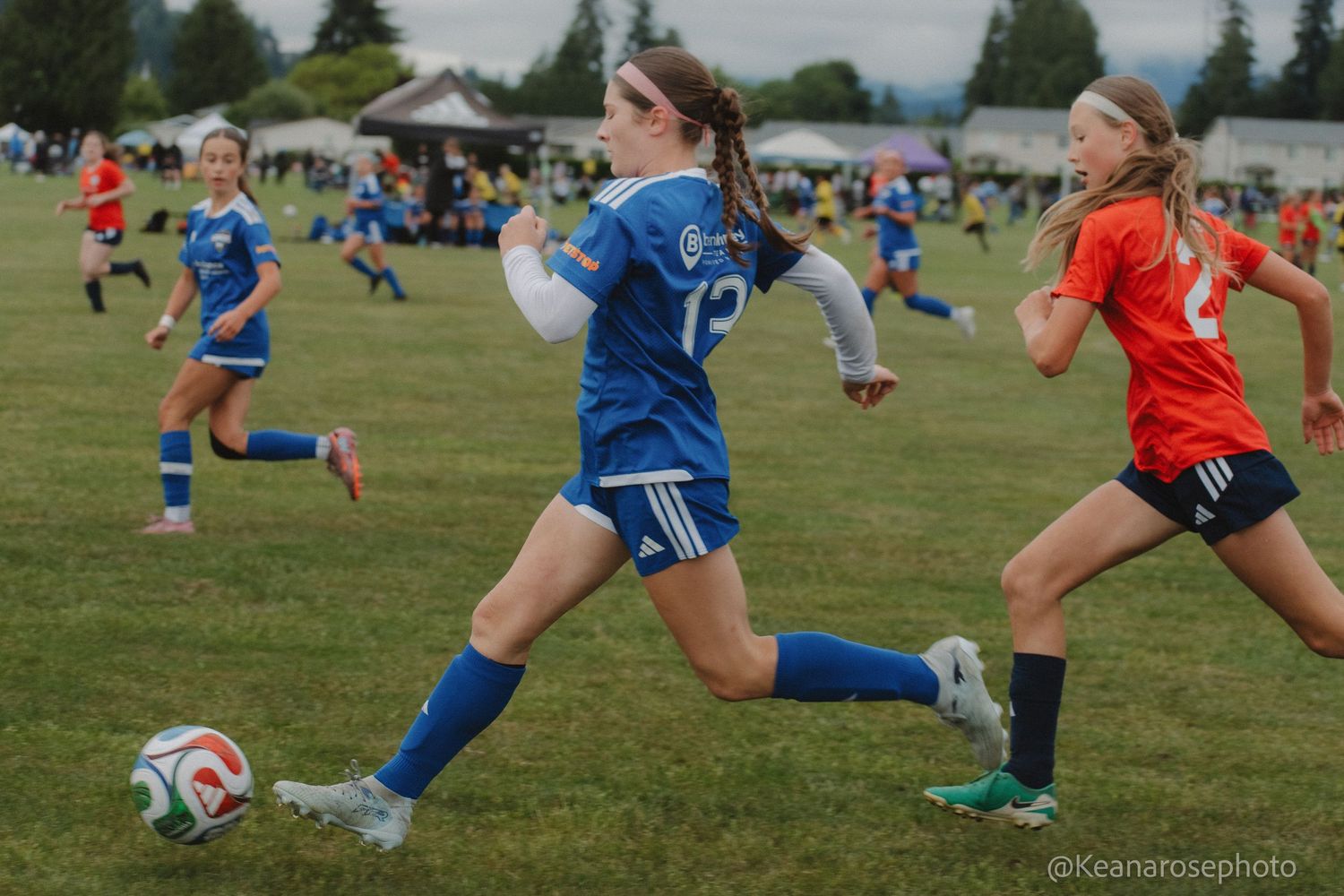 Young female soccer player in blue uniform dribbles ball during an outdoor youth soccer tournament.