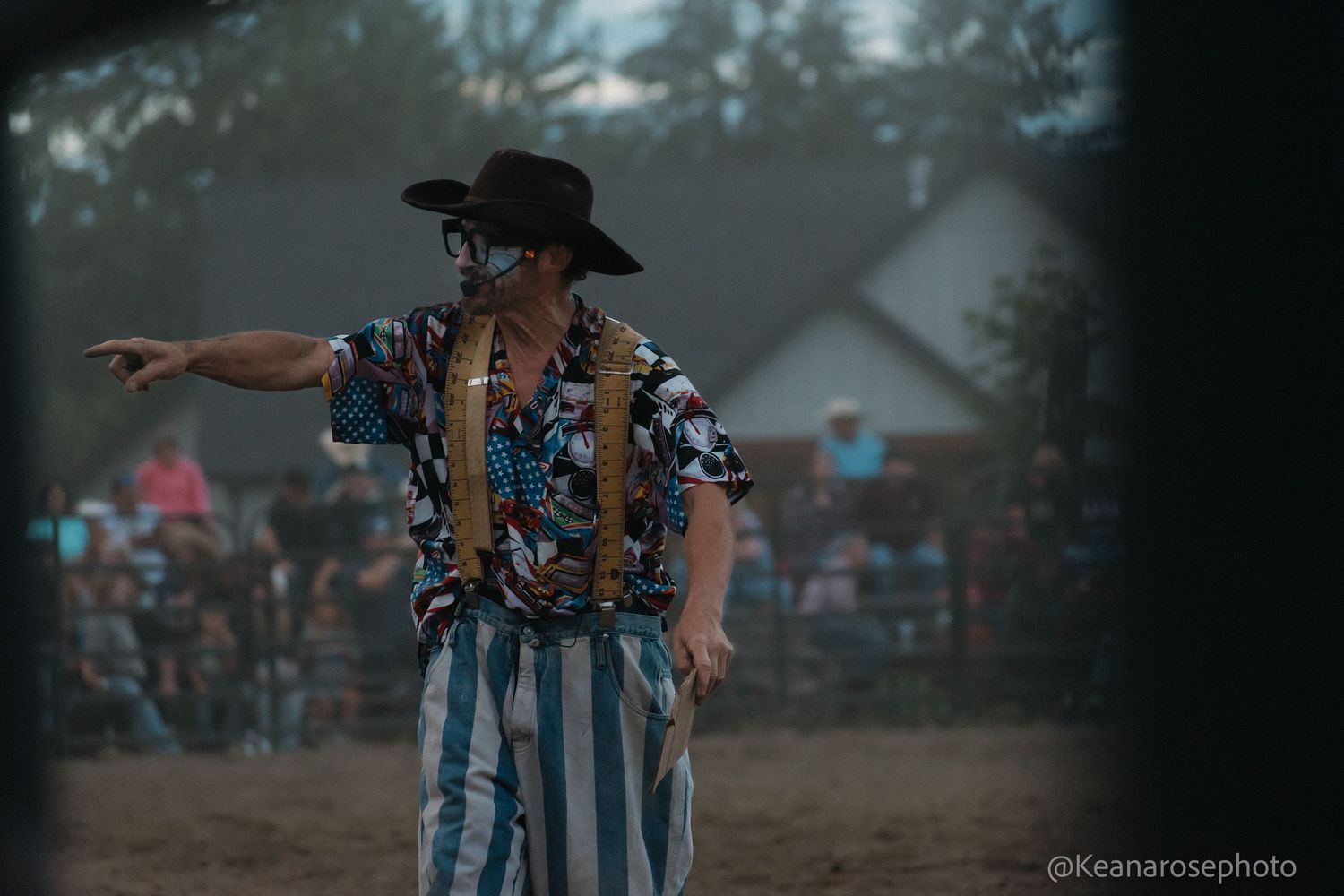 Rodeo clown in striped pants and floral shirt points to crowd during a rodeo performance.
