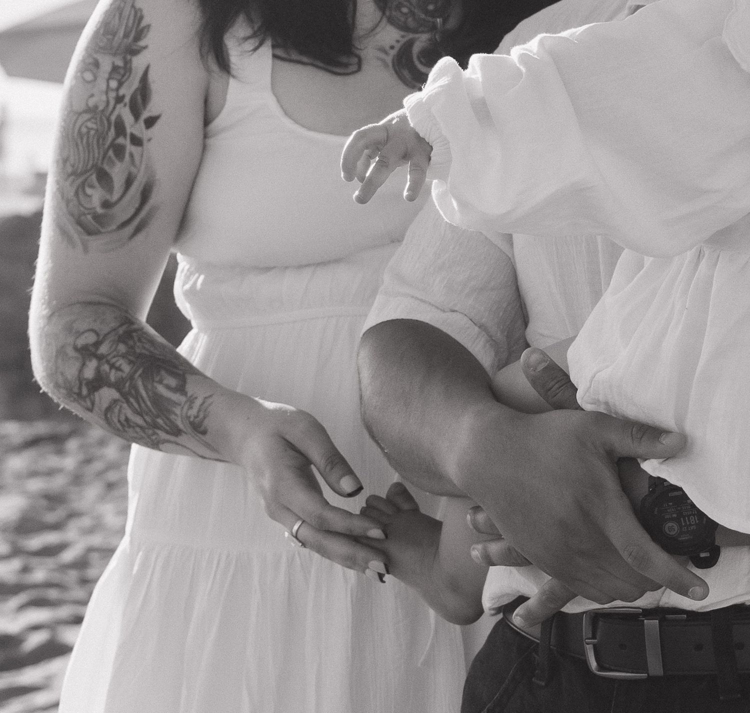 Black and white photo of tattooed couple holding hands, woman in white dress, man in white shirt, exchanging rings.