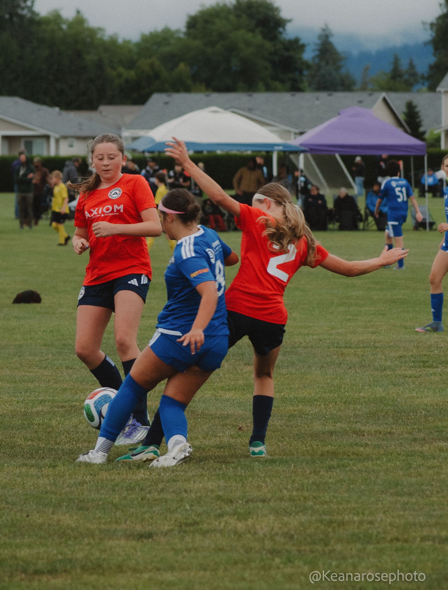 Girls soccer players in red and blue uniforms compete for the ball during an outdoor youth tournament game.