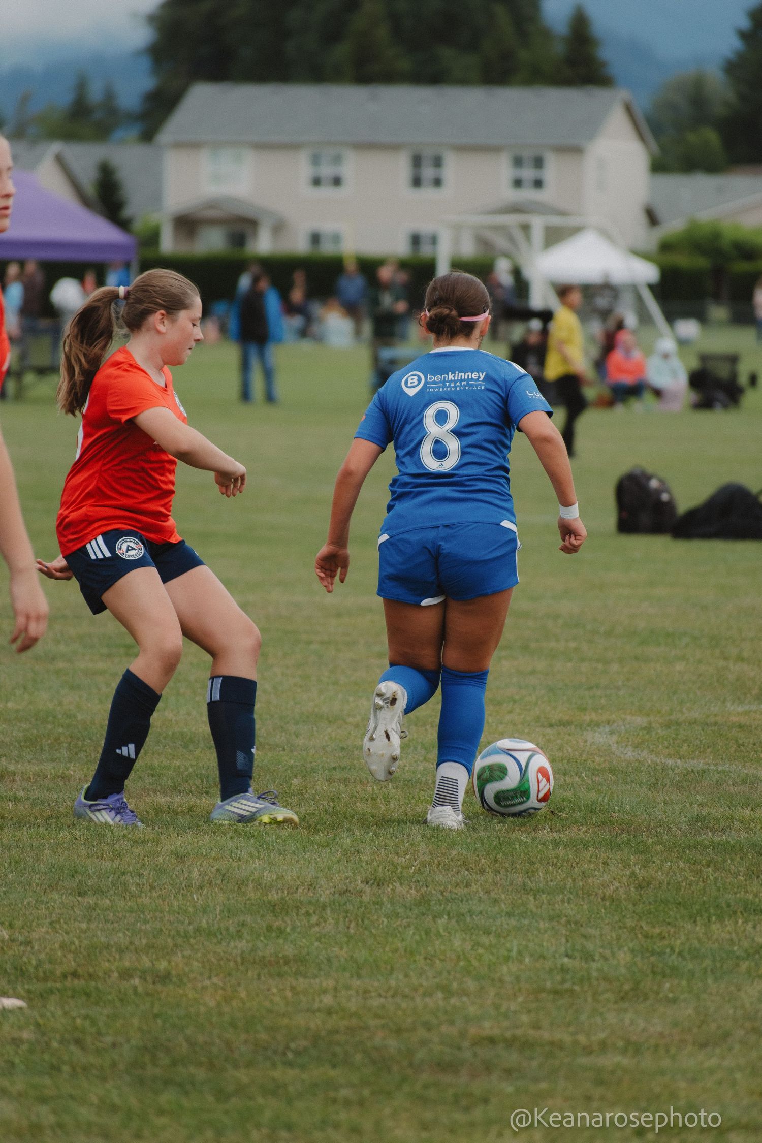 Female soccer players in red and blue uniforms face off during an outdoor youth soccer tournament game.