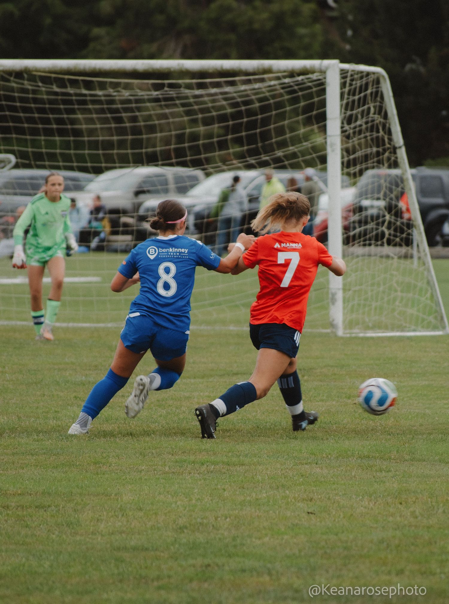 Female soccer players in blue and orange uniforms battle for the ball near the goal during a match.