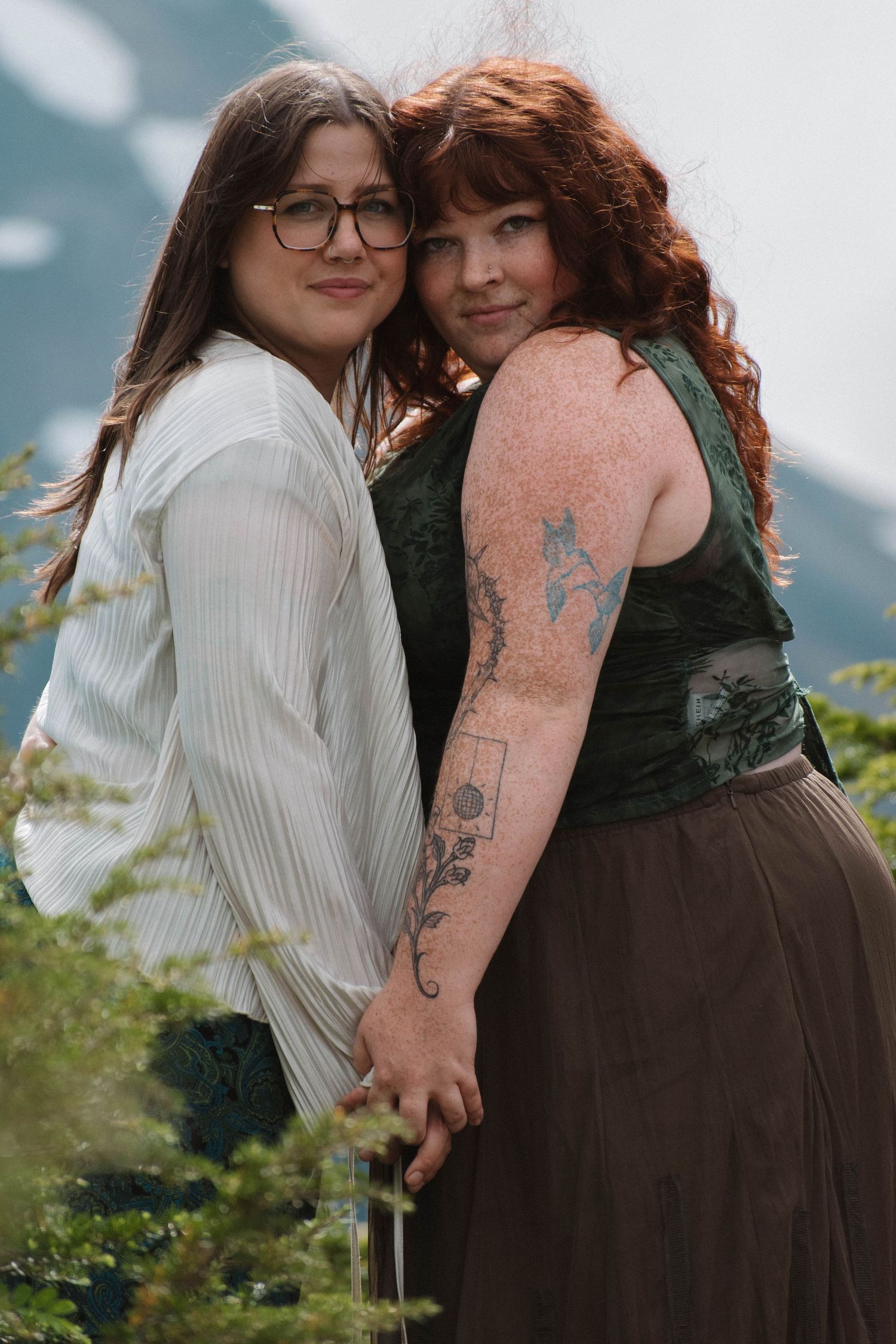 Two women holding hands and posing together on mountain with stunning landscape background.