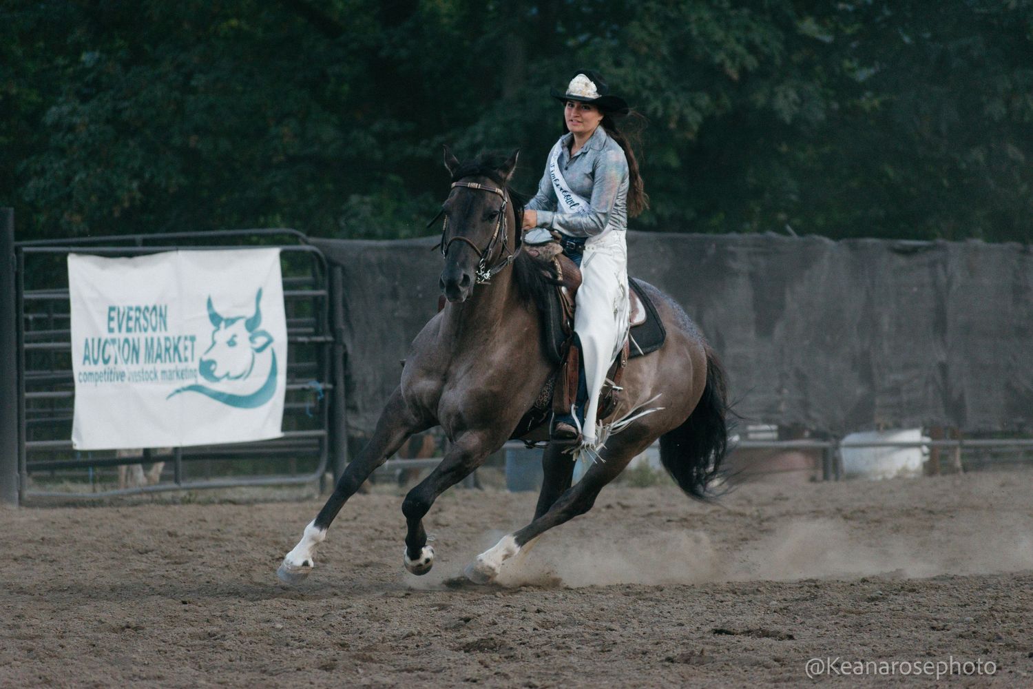 Rider on dark horse performs sliding stop in dusty arena at Everson Junction Ranch event.