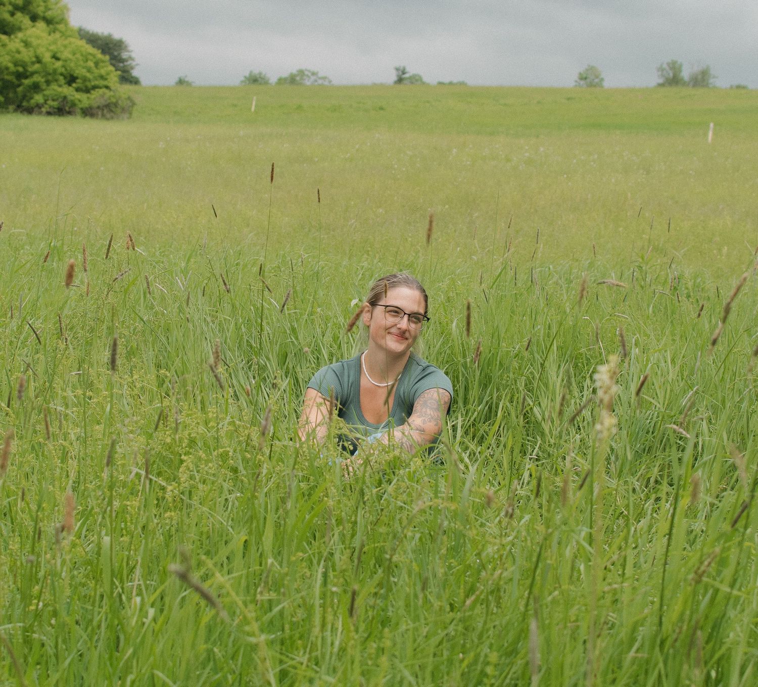 Woman smiling in a lush green field of tall grass on a cloudy day.
