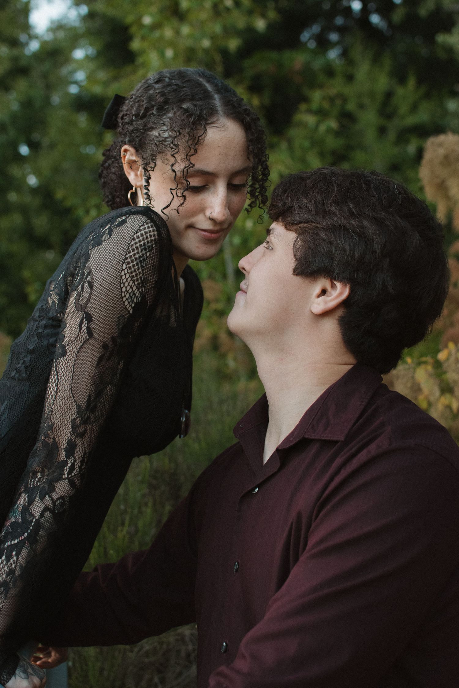 Young couple in dark attire sharing an intimate romantic moment in lush green garden.