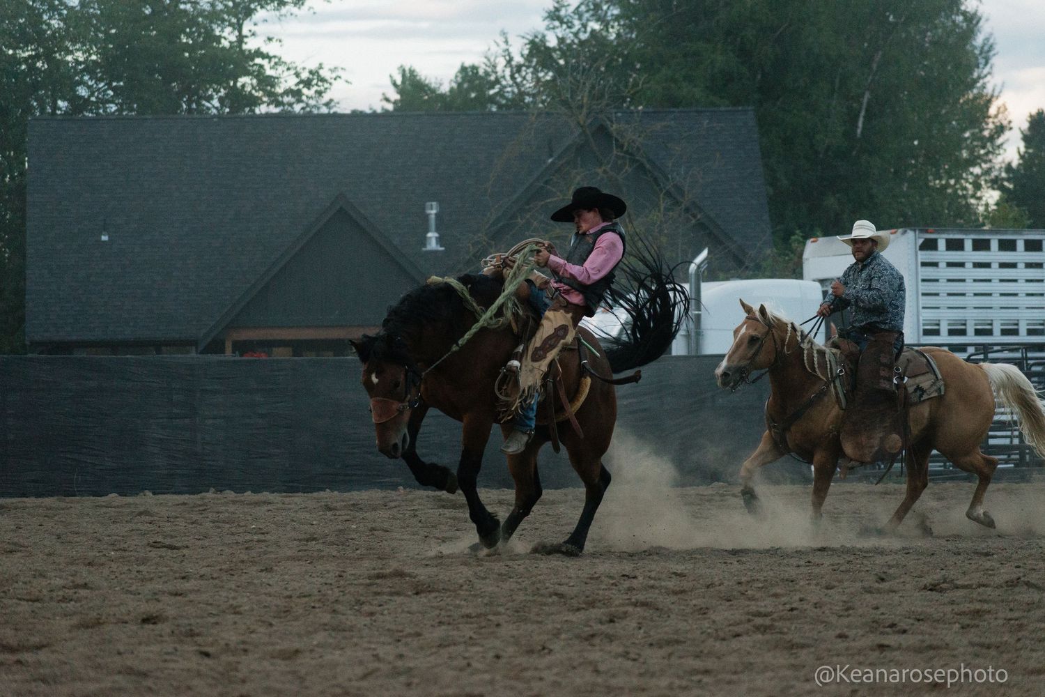 Cowgirl in pink riding a bucking horse at a rodeo with another rider in the background.