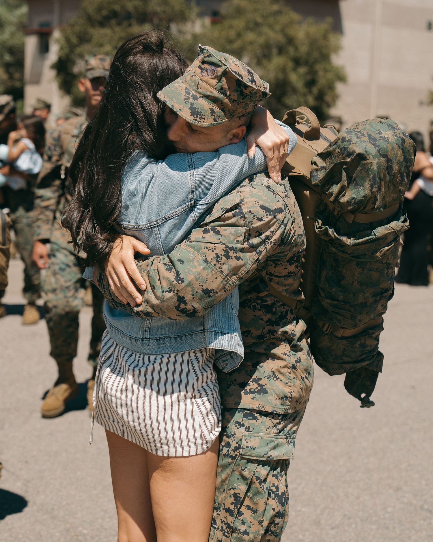 A soldier in camouflage uniform embraces a woman in a heartfelt military homecoming reunion outdoors.
