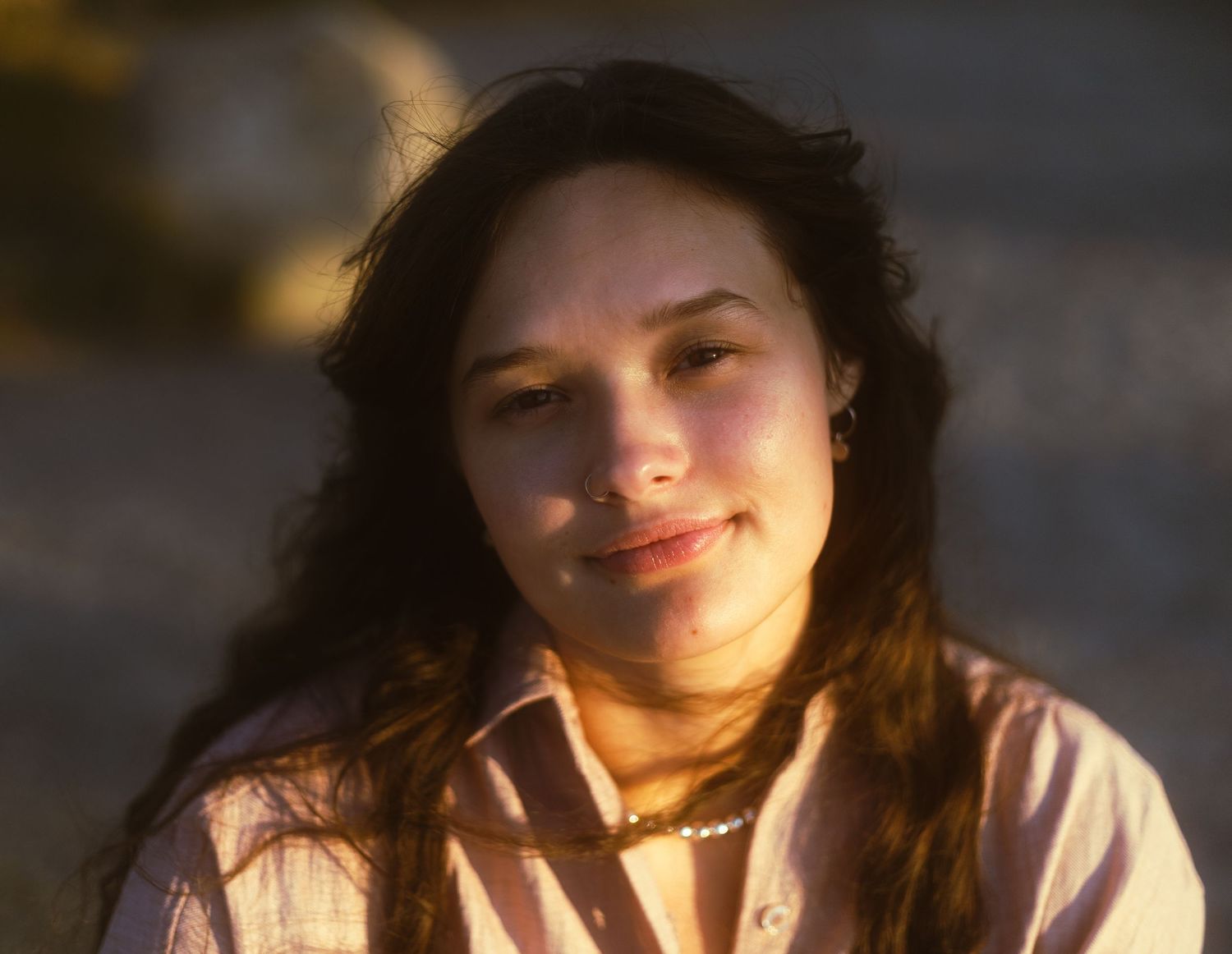 Young woman with curly dark hair smiles softly in warm golden sunlight outdoors.