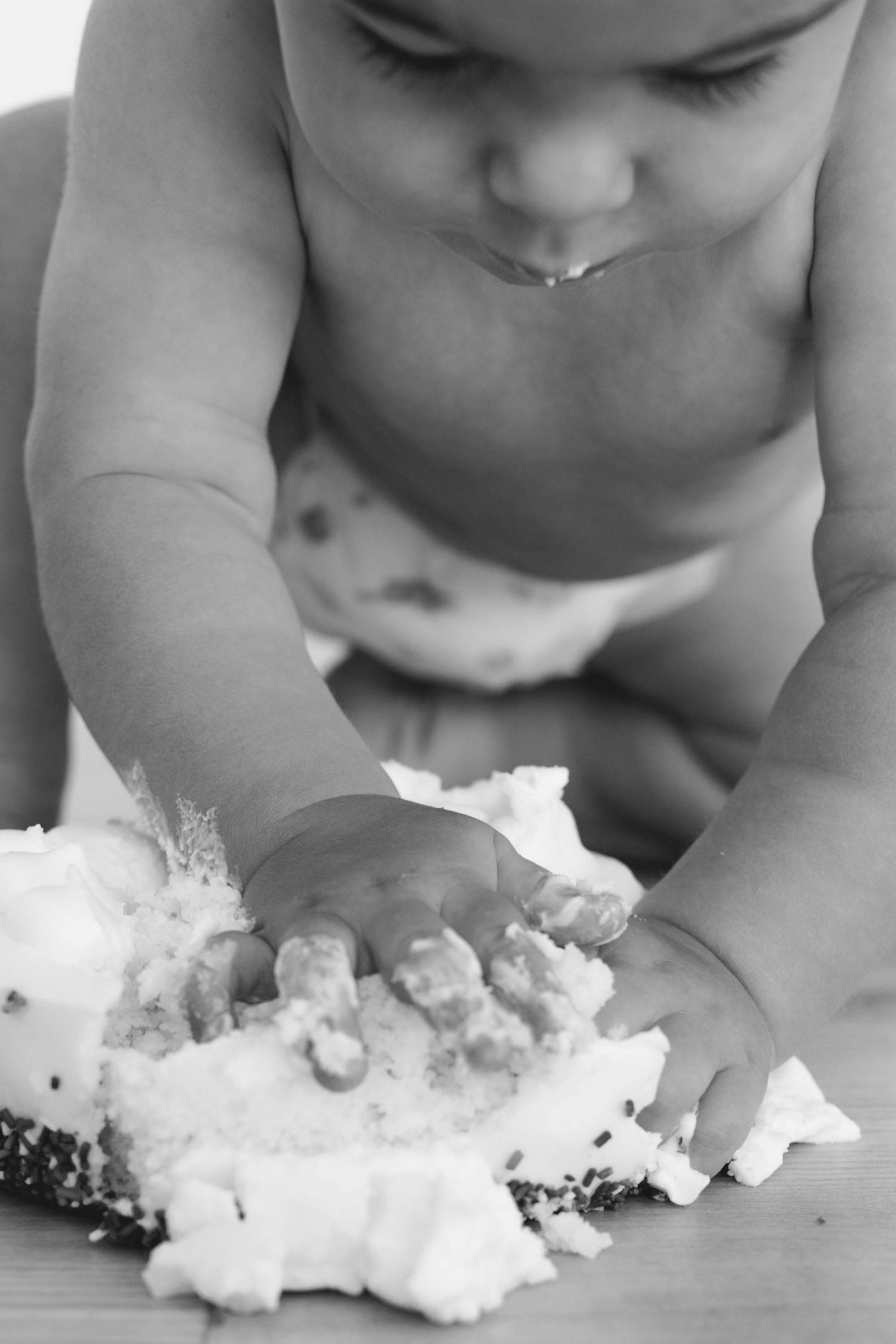 Black and white photo of a baby smashing a white frosted cake with their hands.