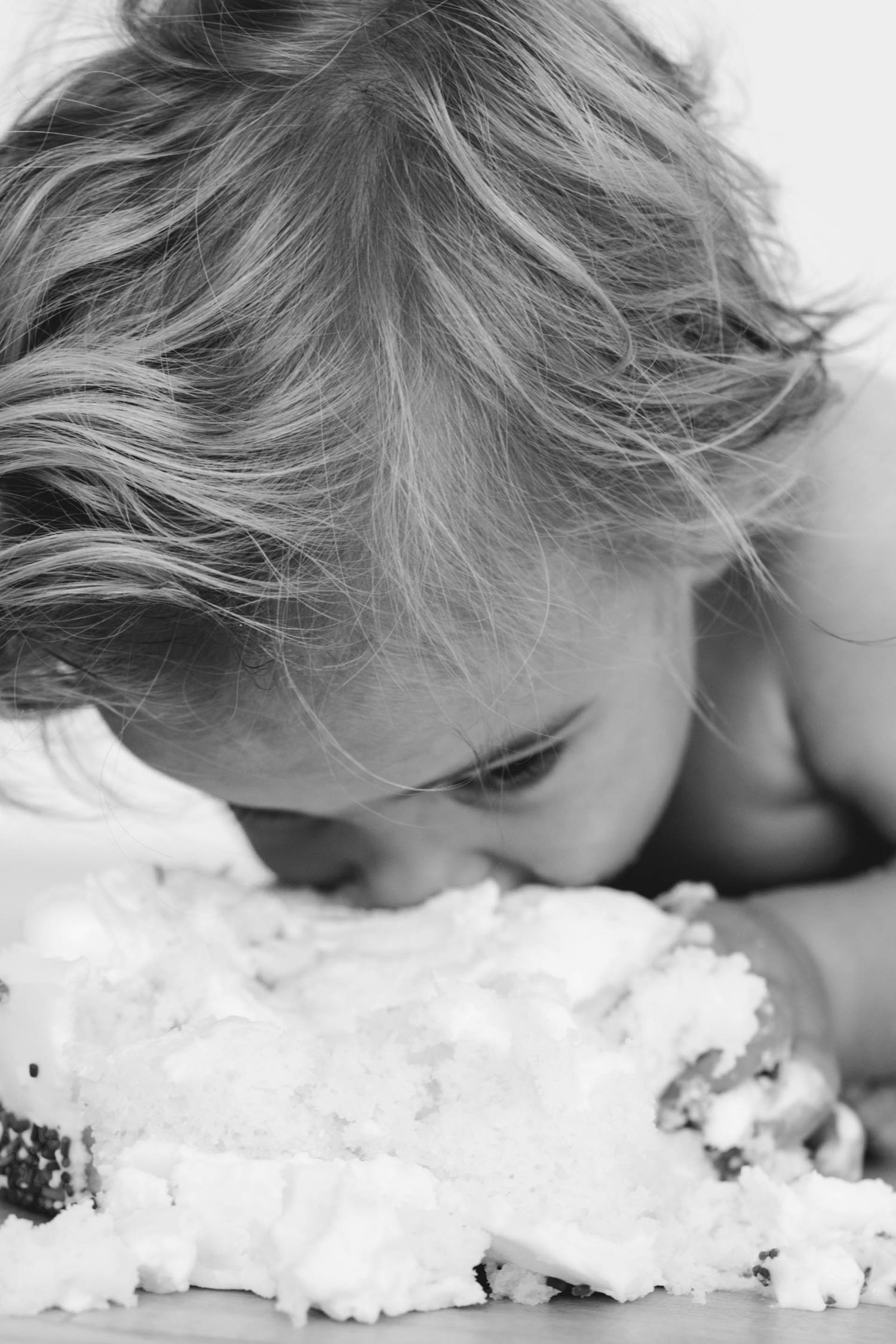 Black and white close-up of a young child smashing their face into a birthday cake.