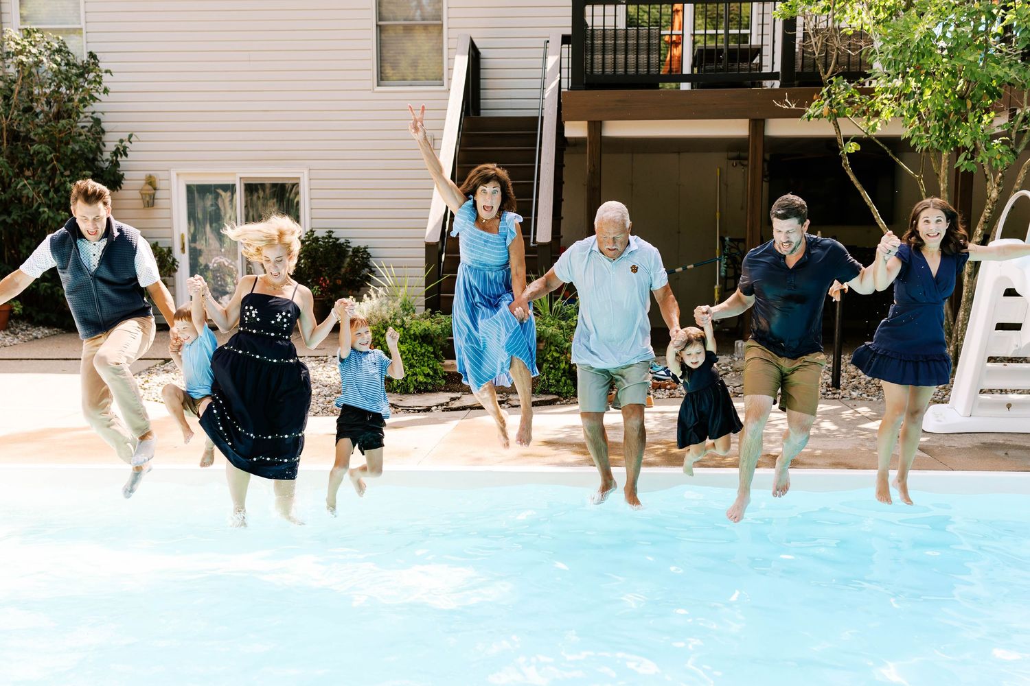 Extended family group joyfully jumps into a backyard swimming pool together on a sunny day in St.Louis.