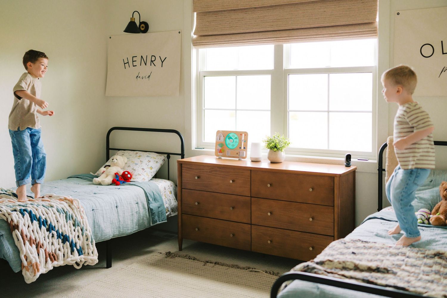 Two young boys jump on their beds in a shared bedroom decorated with name signs and colorful bedding.