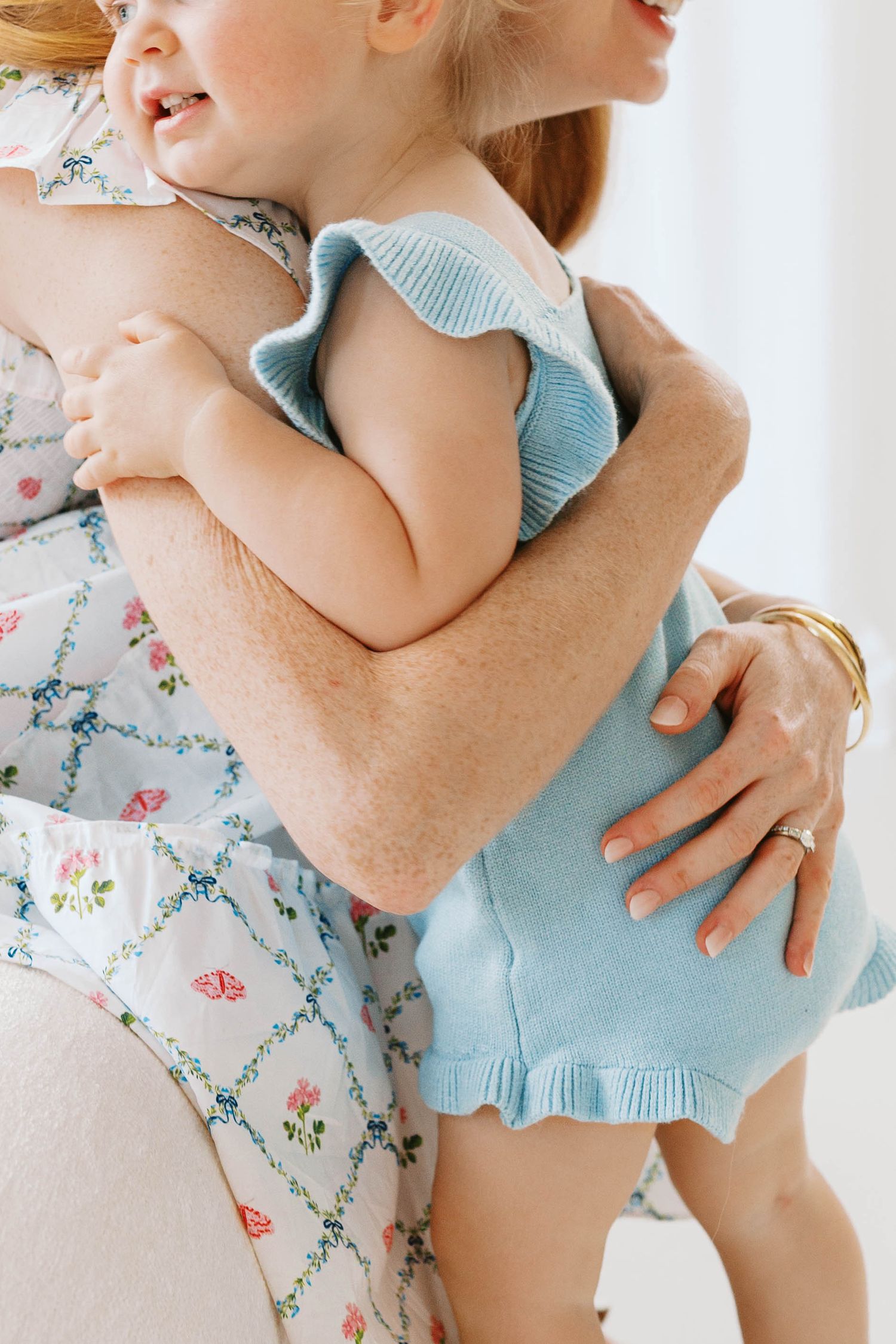 Mother tenderly holding baby dressed in blue knit romper in a bright, airy setting.