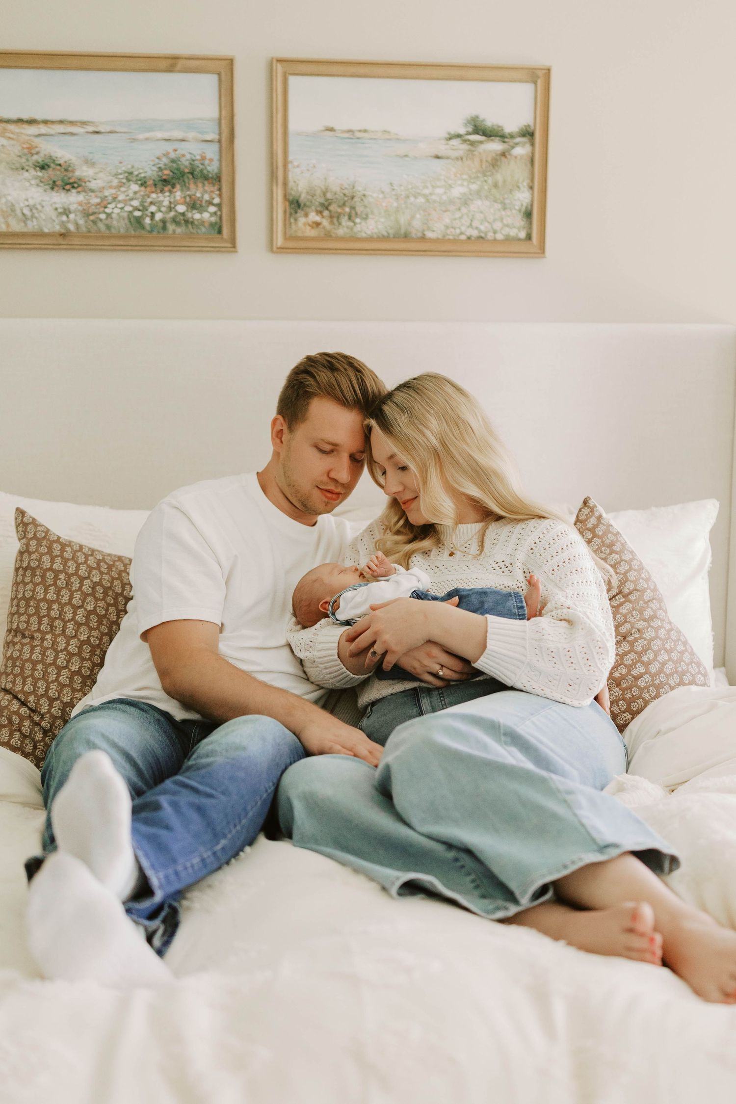 Couple gazes lovingly at their newborn baby while sitting together on a white bed during an in home newborn session.