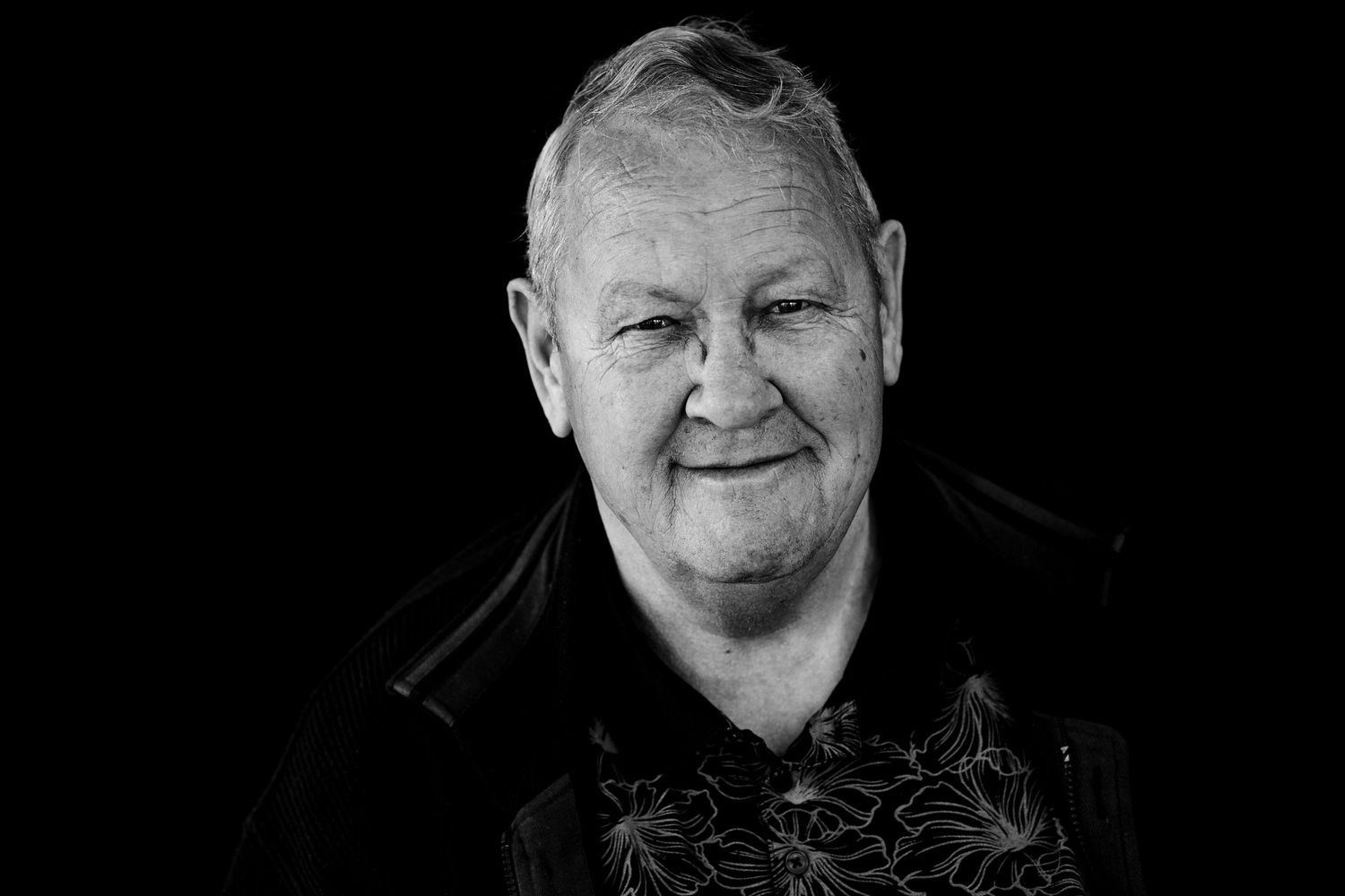 Black and white portrait against dark background showing person wearing dark clothing with palm tree pattern.