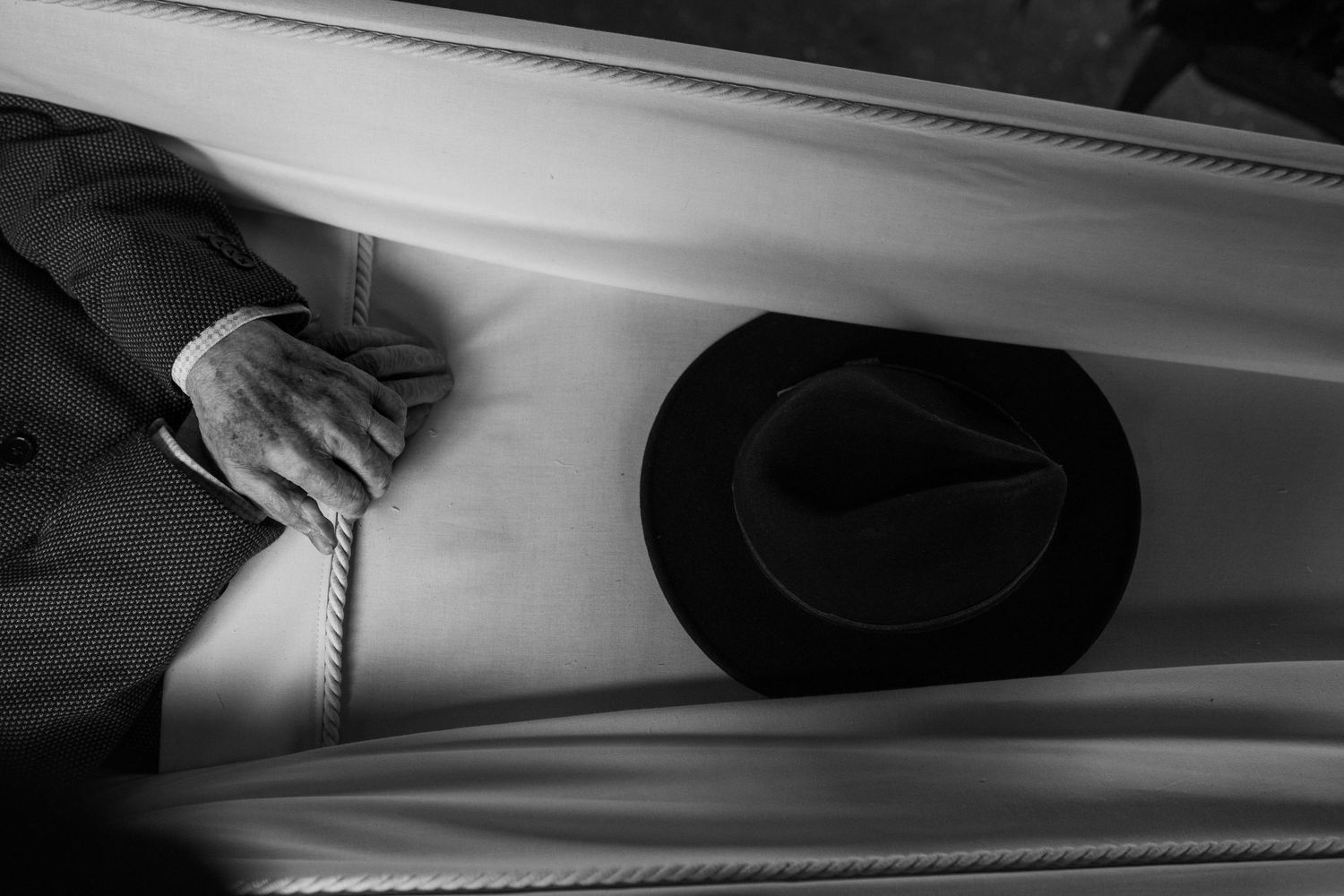 Black and white image of a hand next to a cowboy hat on a light surface.