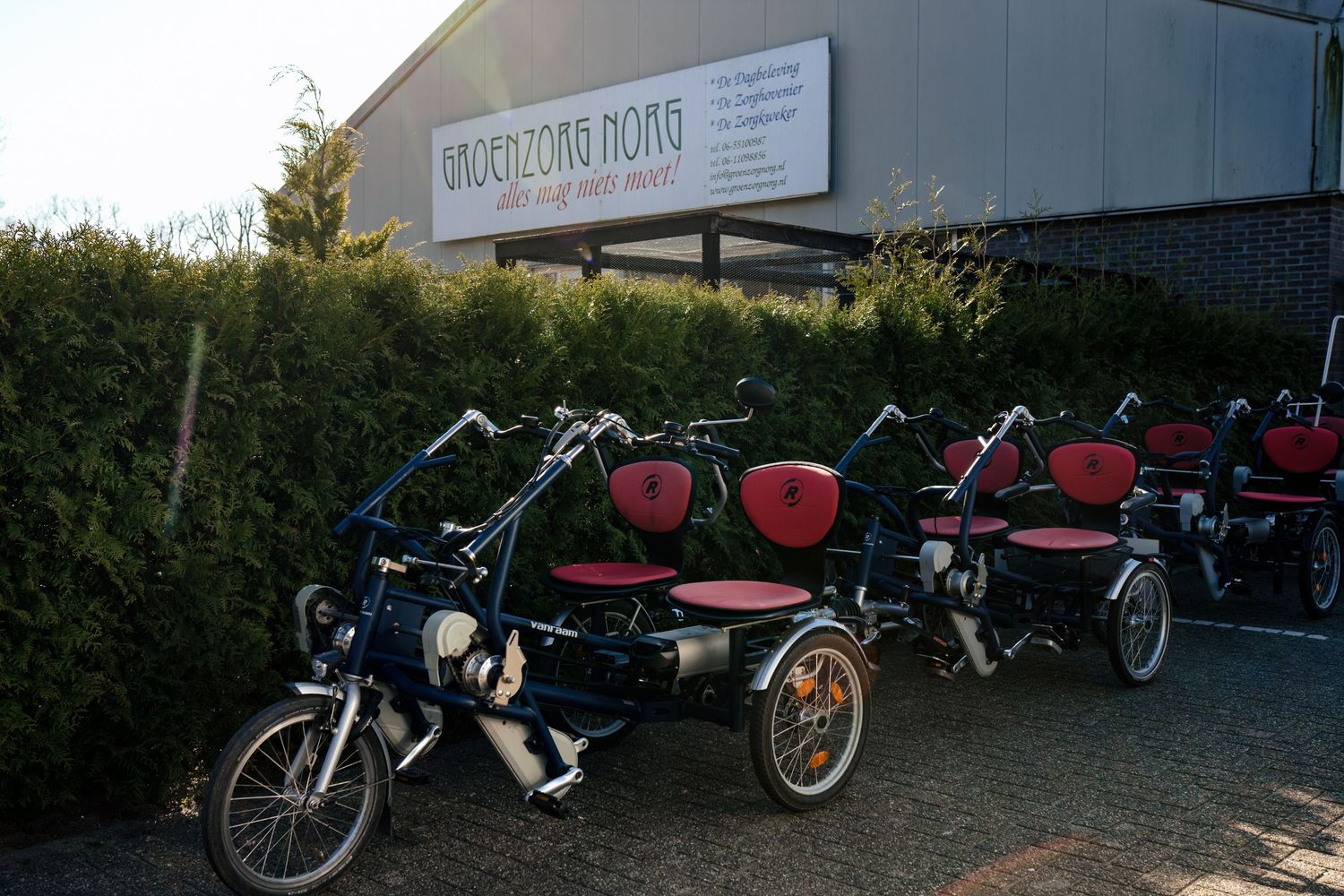 Row of mobility scooters and adaptive bikes parked outside a building.