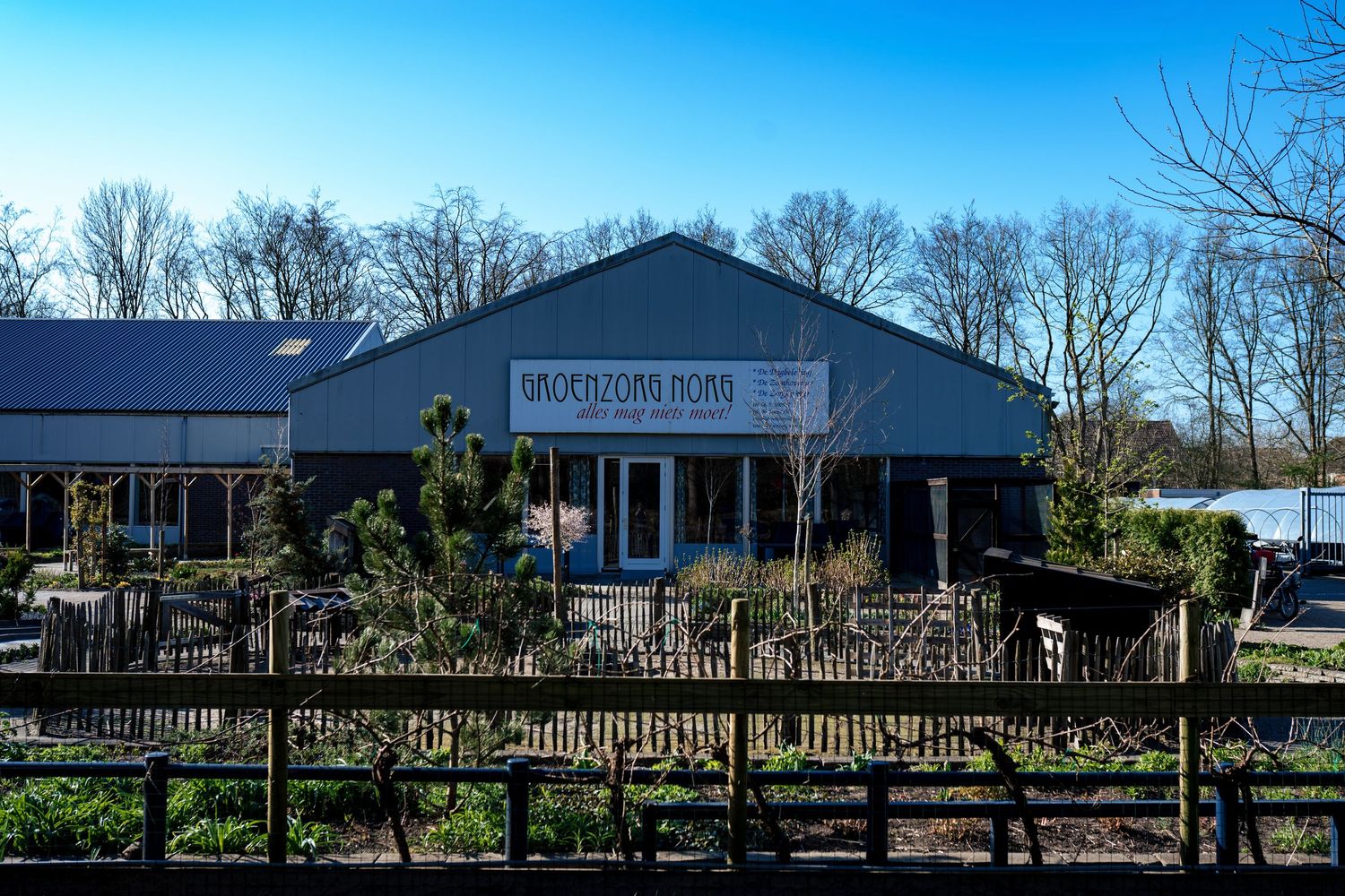 Exterior view of a building with wooden fence and landscaping under bright blue sky.