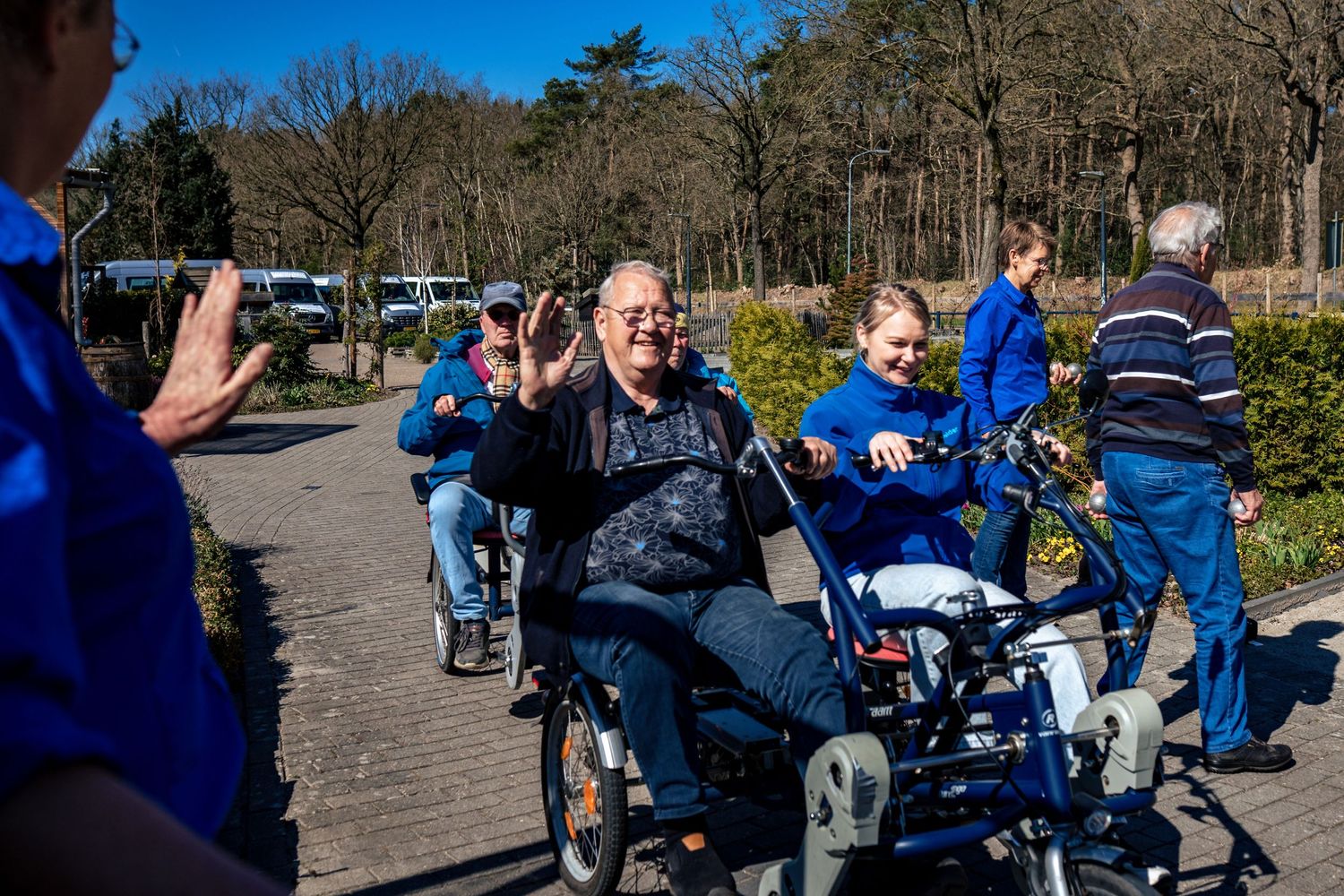 Group of people on mobility devices gathering outdoors on a sunny day with trees in background.