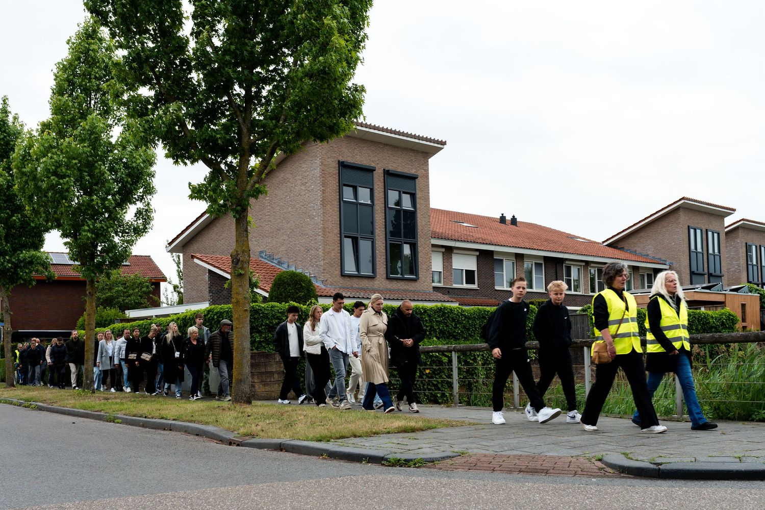 Large group of people walking along a path outside residential buildings.