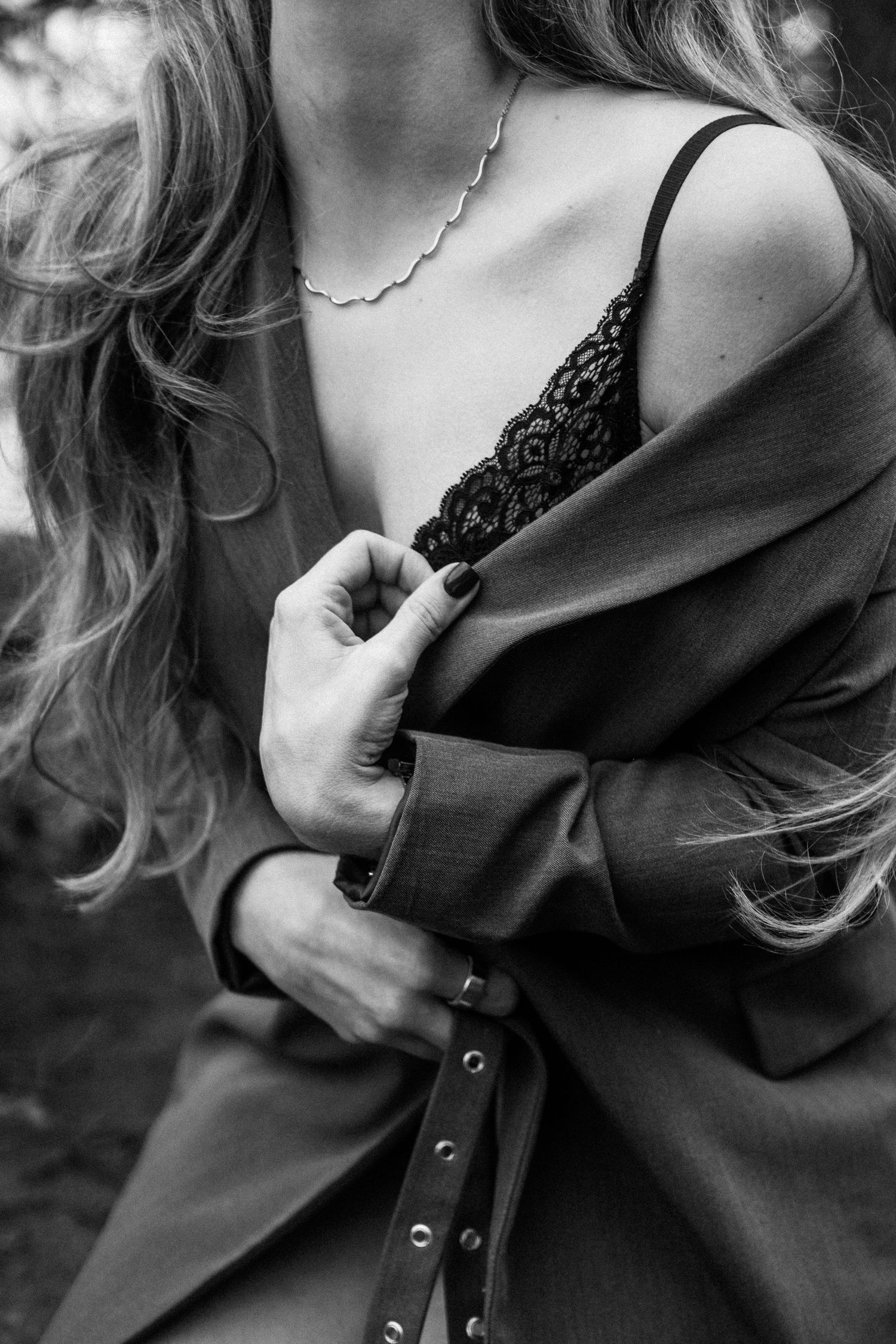 Black and white close-up of woman in lace bralette and oversized blazer holding lapel outdoors. By Soft Sacred Studios.