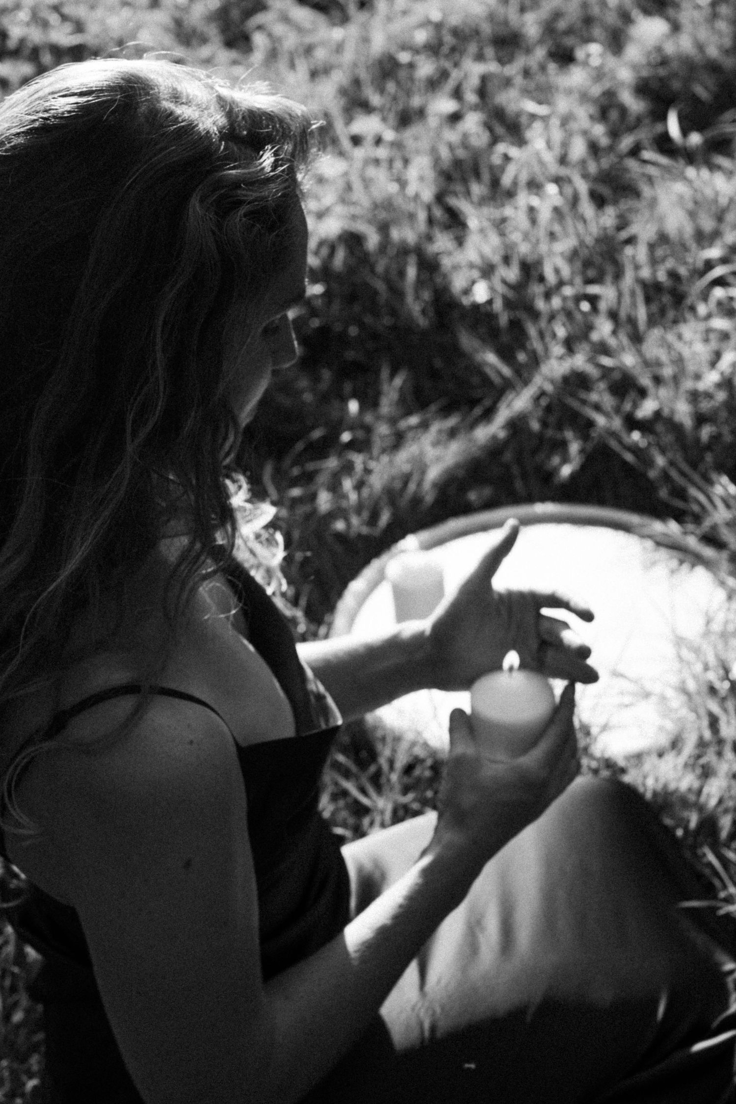 Black and white photo of woman holding a lit candle while sitting outdoors in nature. By Soft Sacred Studios.