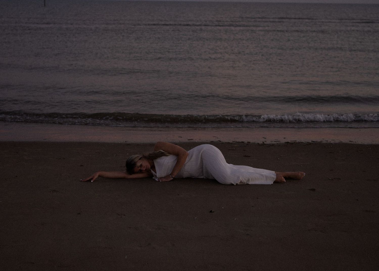Woman lying on dark beach in white clothing - fine art feminine photography, Sacred Water Ceremony photoshoot by Soft Sacred Studios