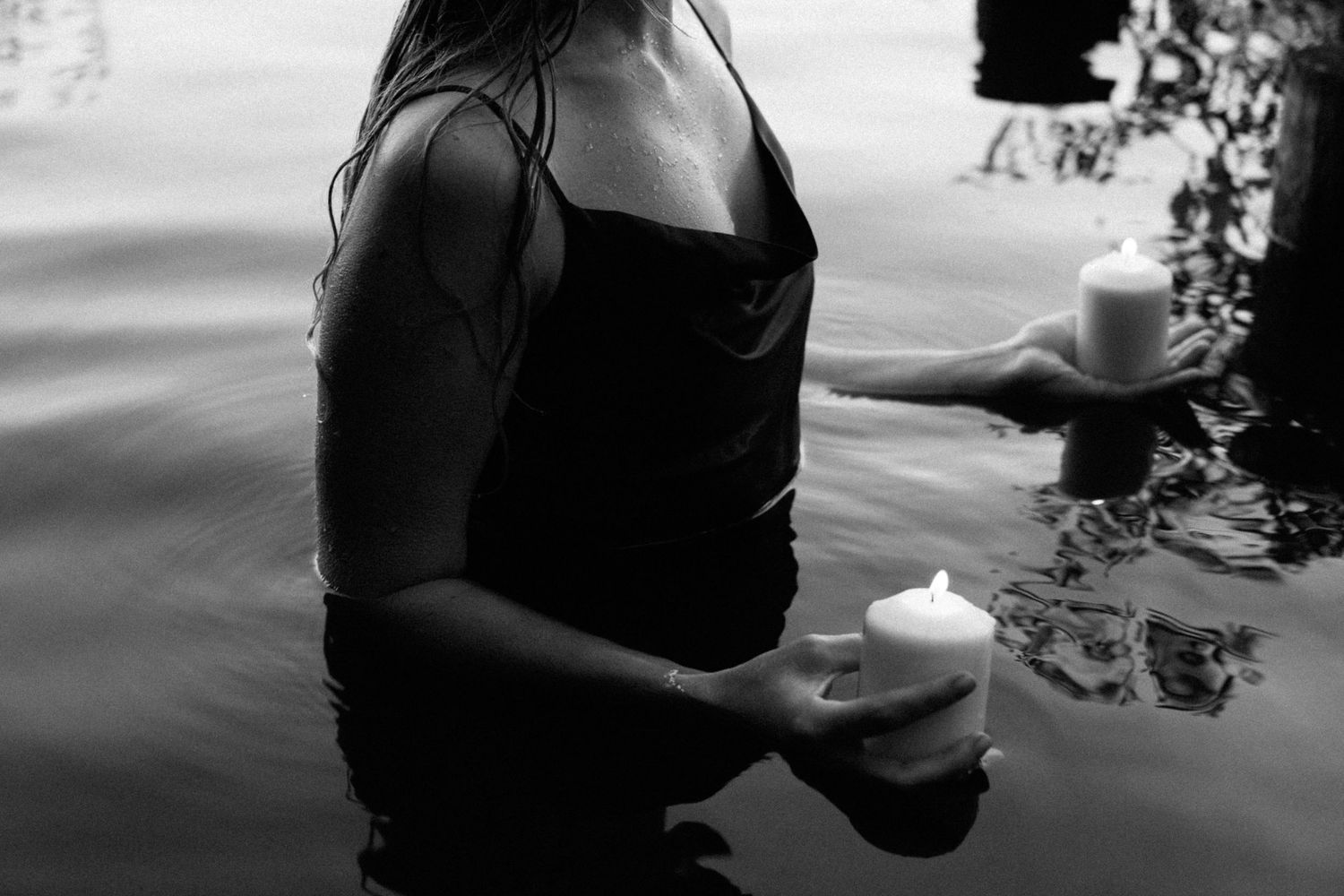 Woman standing in water holding two white pillar candles, black and white artistic photography. By Soft Sacred Studios.