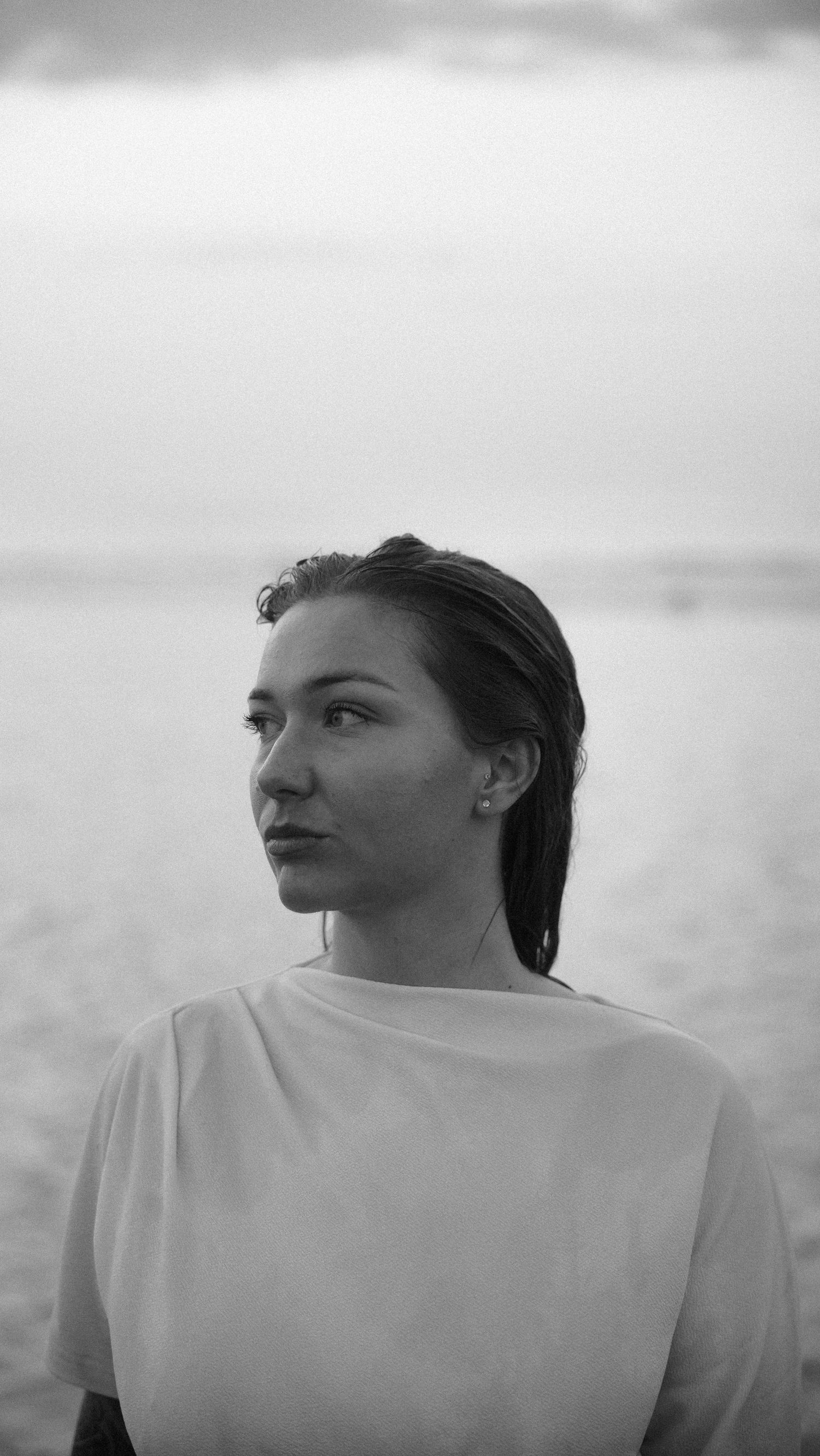 Black and white portrait of a young woman with wet hair gazing at the sea. By Soft Sacred Studios.