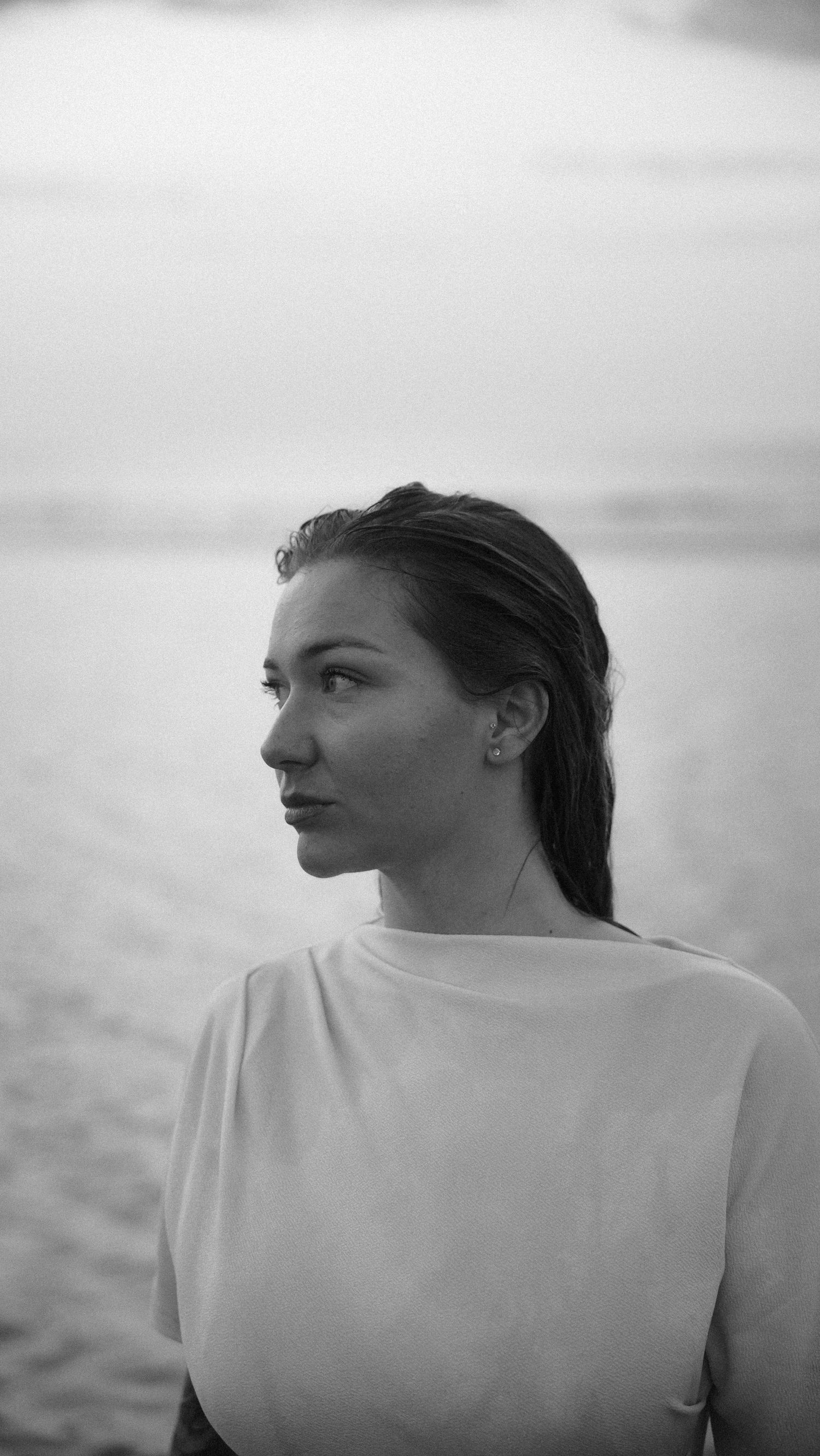 Black and white portrait of a young woman with wet hair gazing at the sea. By Soft Sacred Studios.