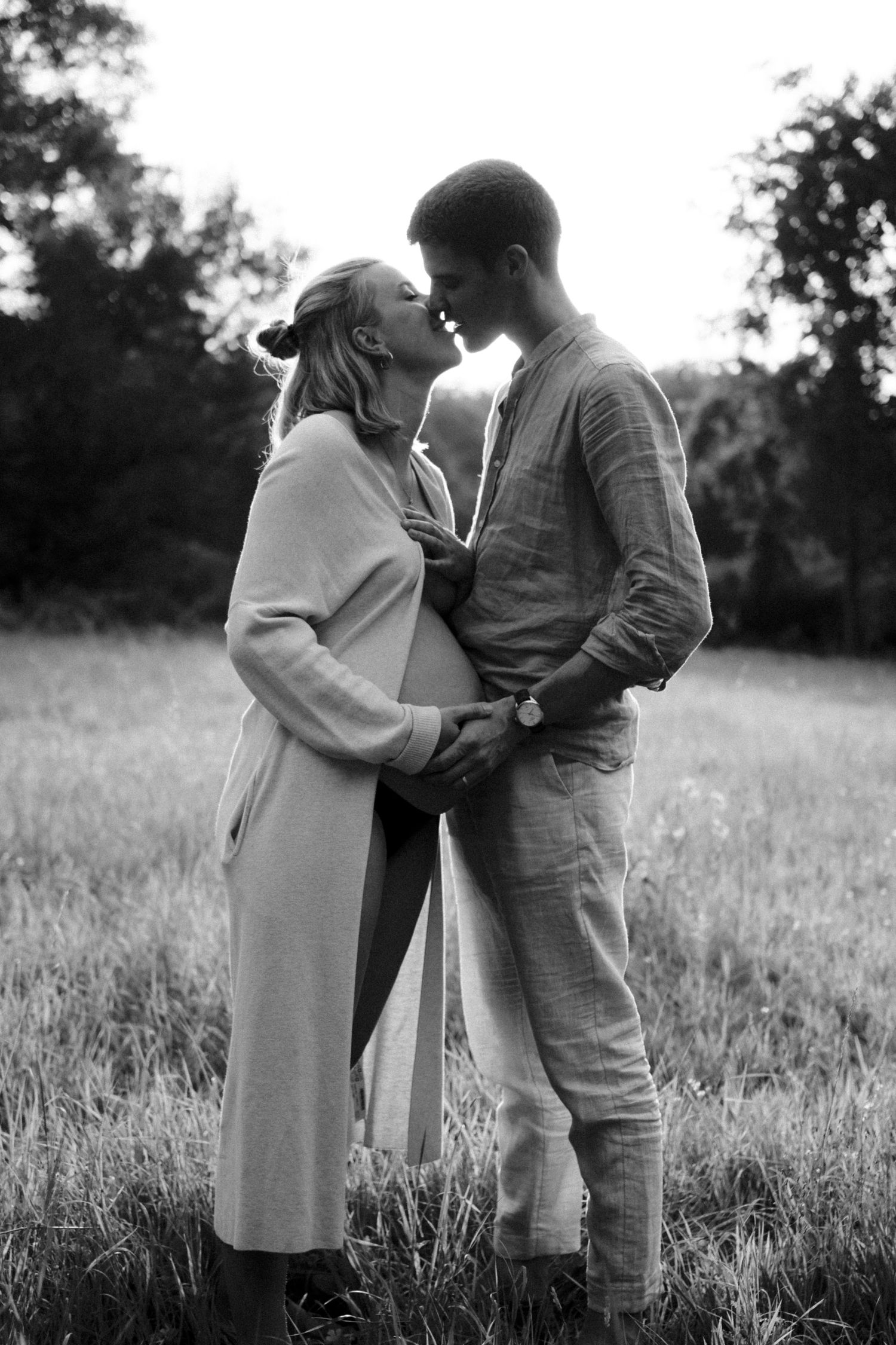 Expectant couple sharing an intimate moment outdoors in a black and white nature portrait. By Soft Sacred Studios.