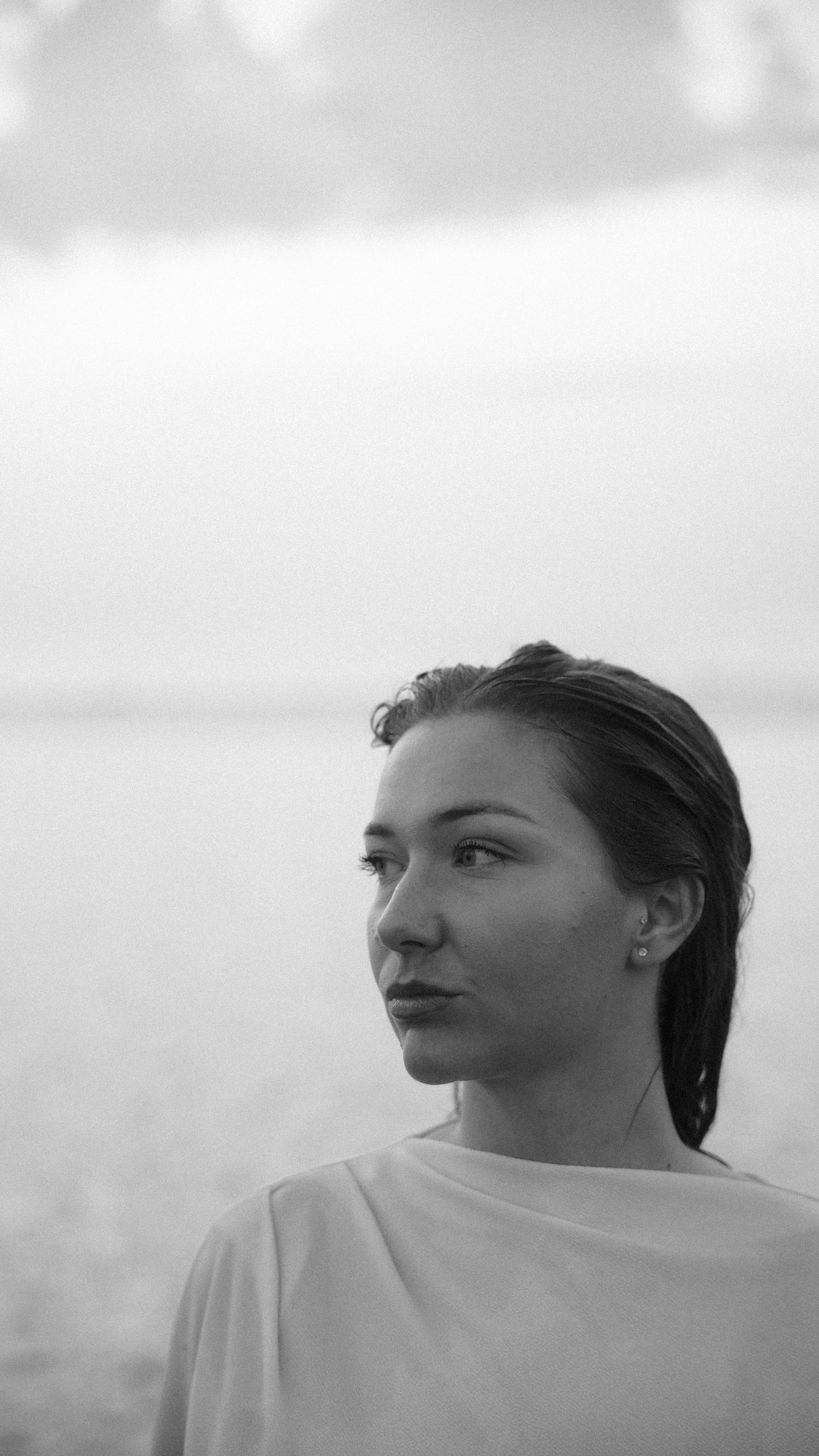 Black and white close-up portrait of young woman with wet hair near ocean shore. by Soft Sacred Studios