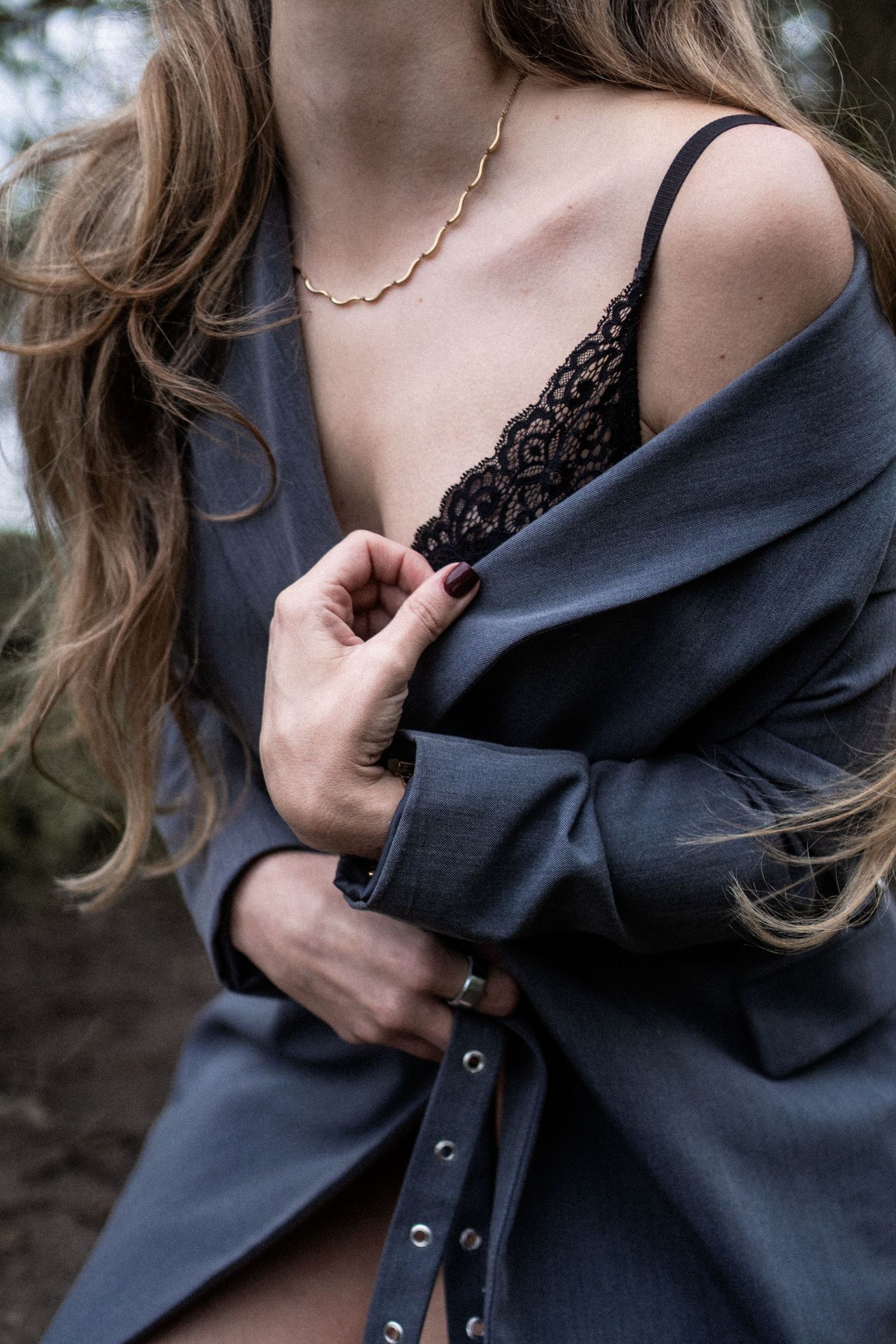 Close-up of a woman in a gray blazer and black lace bralette with a gold necklace outdoors. By Soft Sacred Studios.