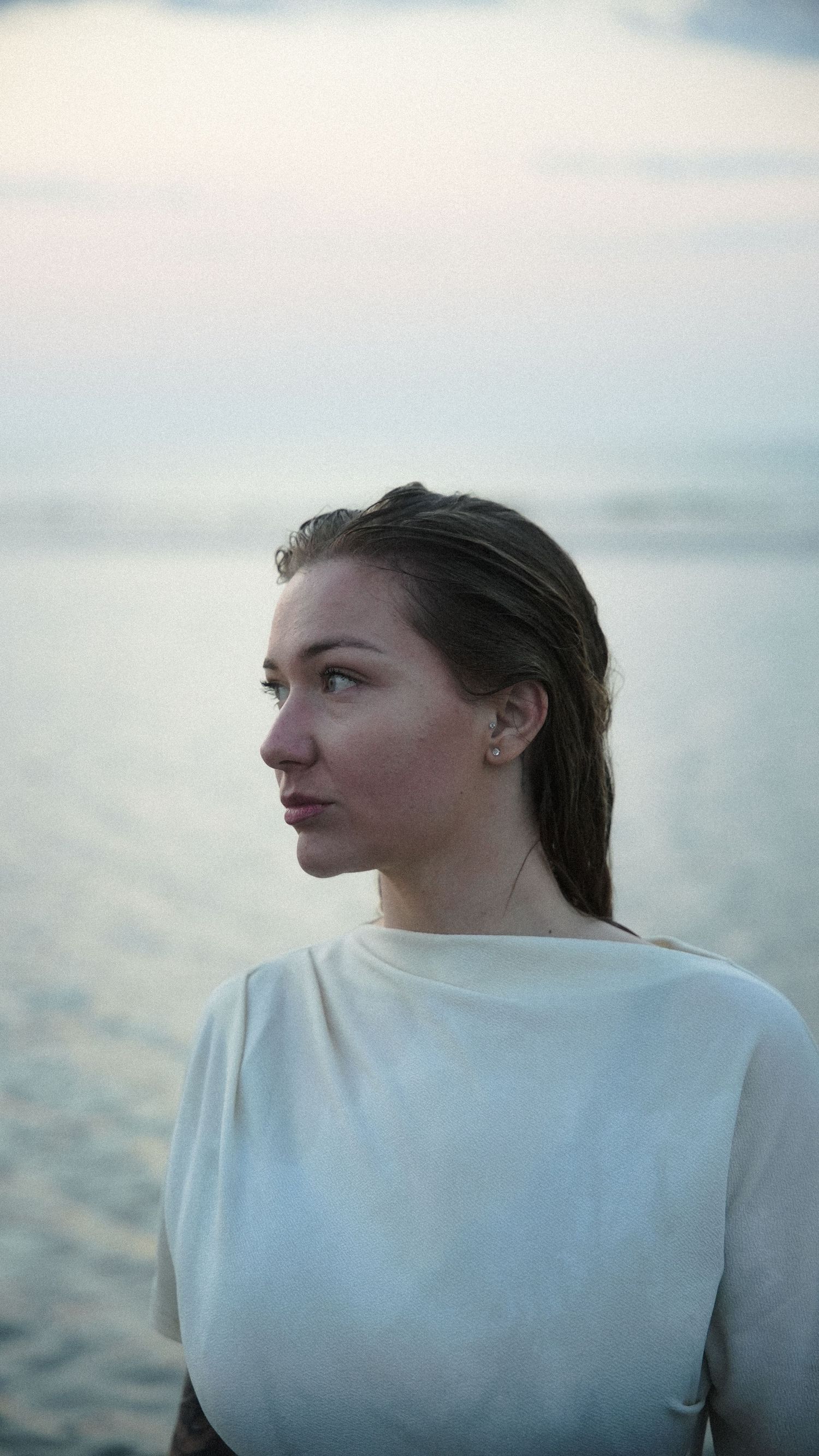 Side profile portrait of young woman in white top at beach during golden hour. by Soft Sacred Studios