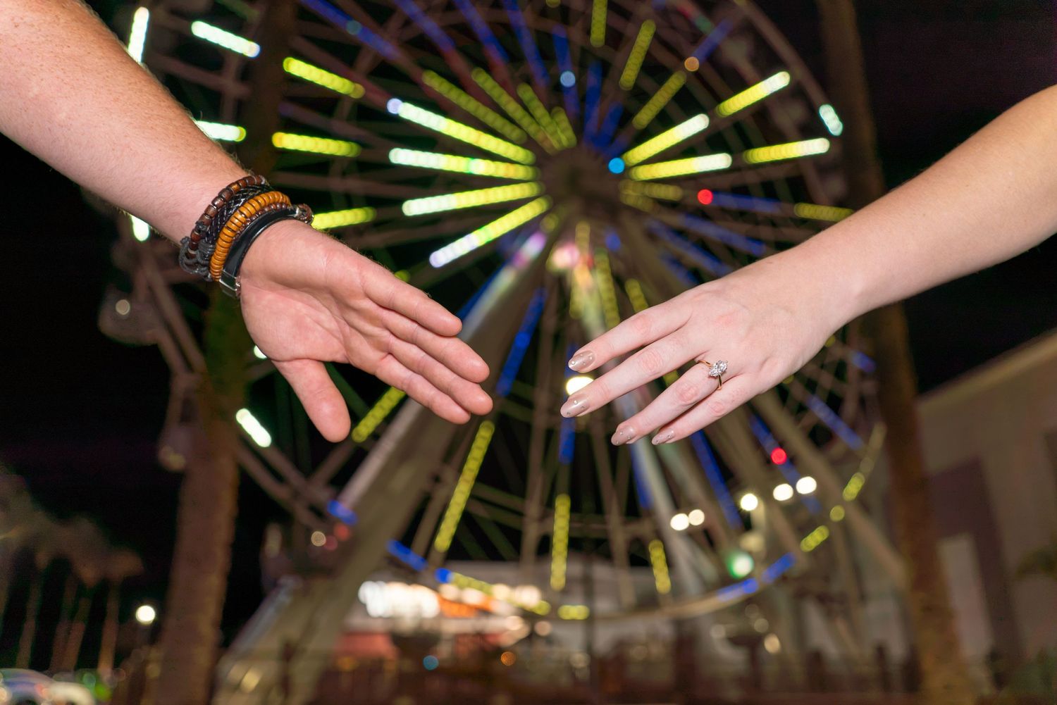 Hands reaching for each other infront of a ferris wheel