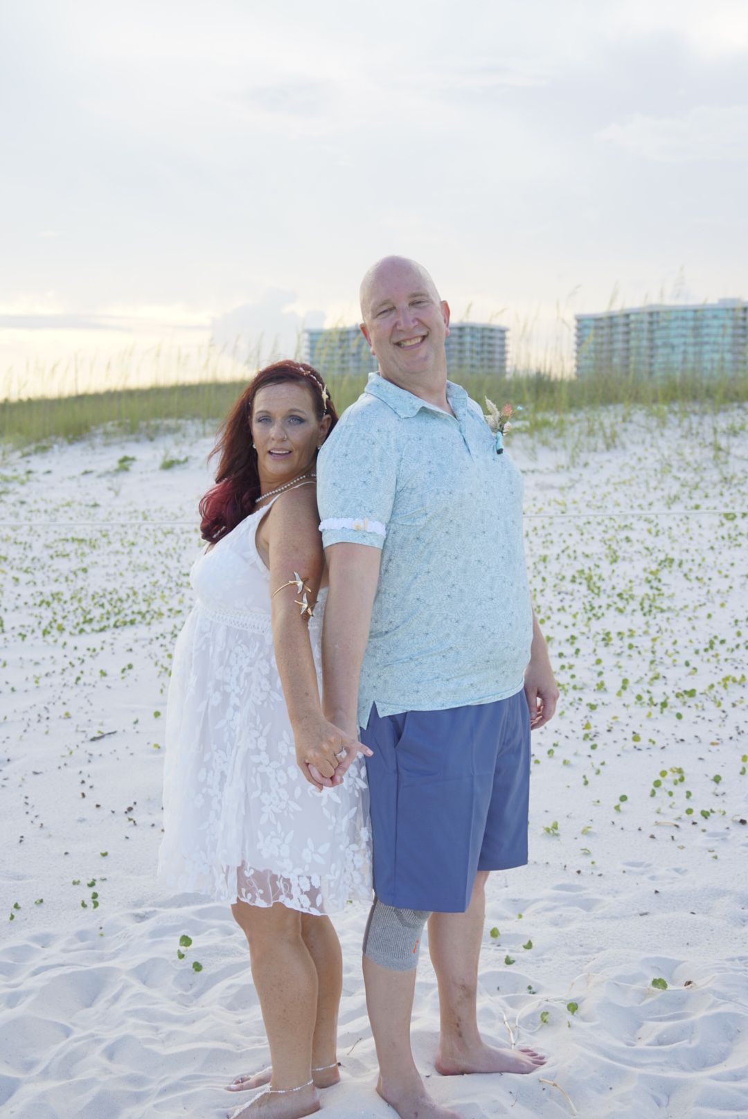 couple stands back to back in front of the dunes