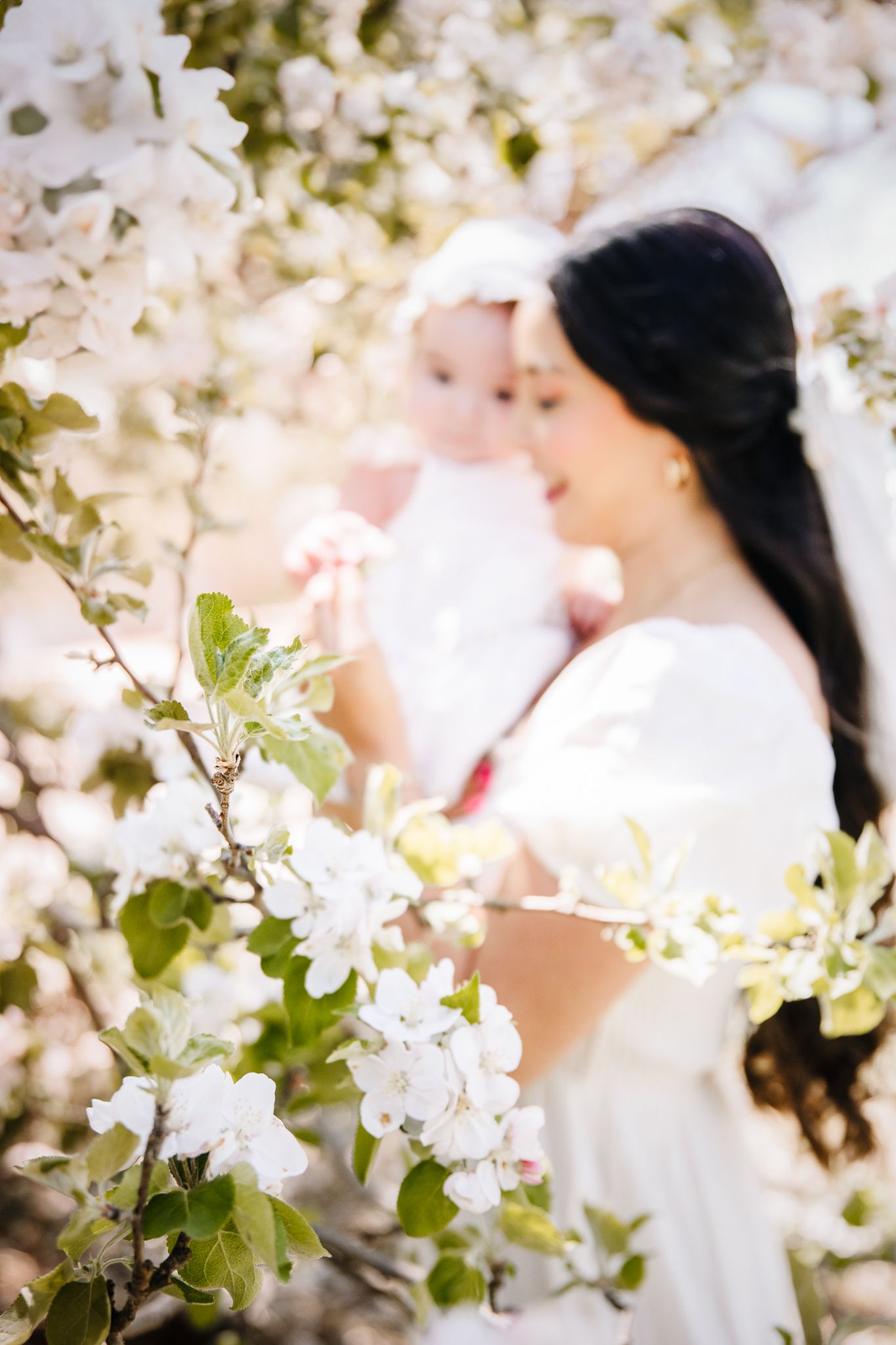 mother and baby daughter looking at spring cherry blossom tree. while they pose for a mommy and me pictures for liz the photographer.