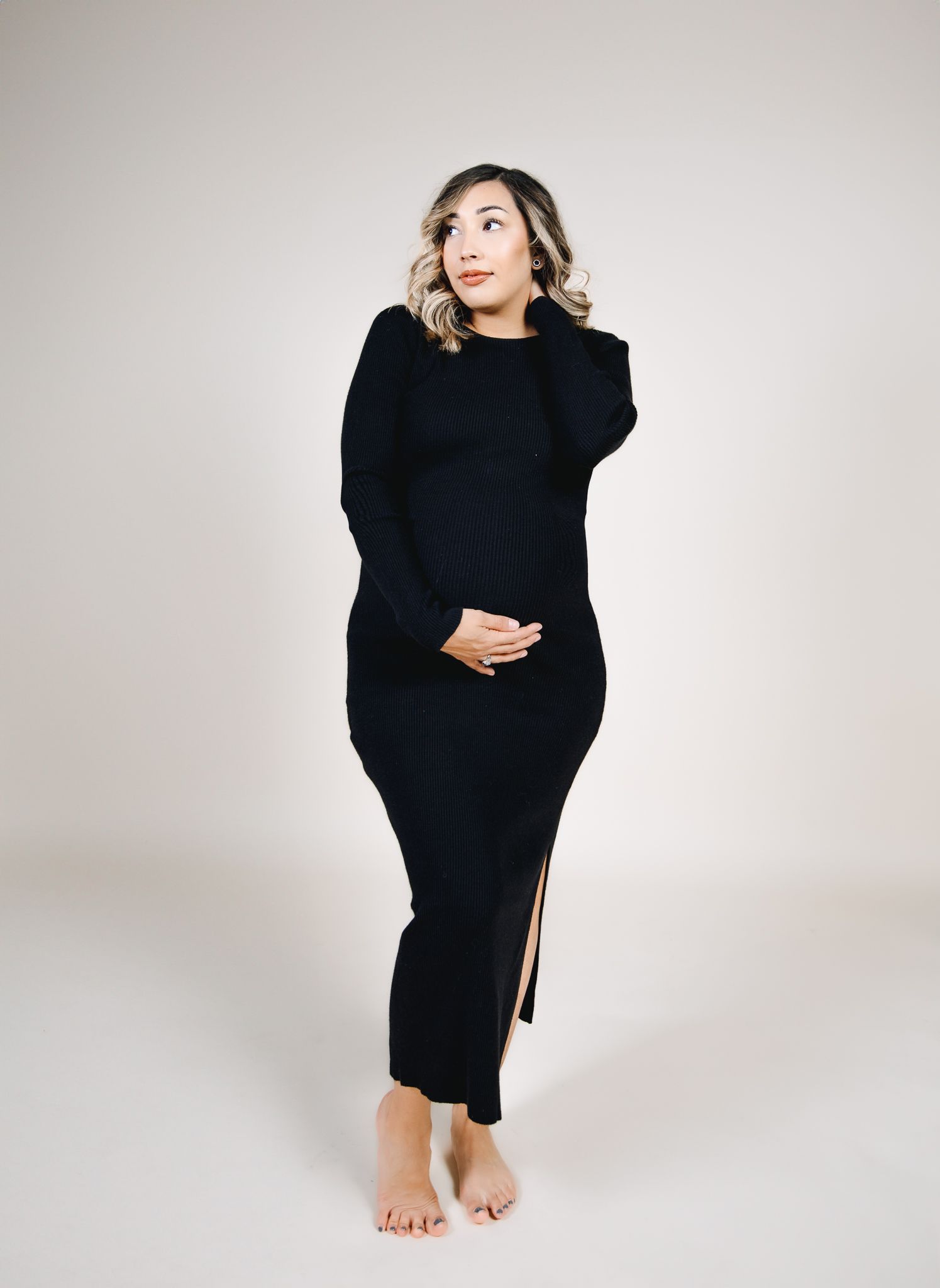 maternity photoshoot with white backdrop and mother holding her belly in a black dress posing for photoshoot in colorado
