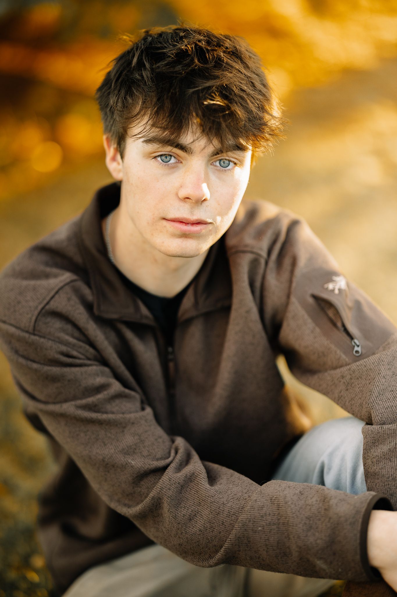 class of 2026 high school senior boy in Windsor Colorado posing for her senior pictures in a blue shirt softly smiling at the photographer