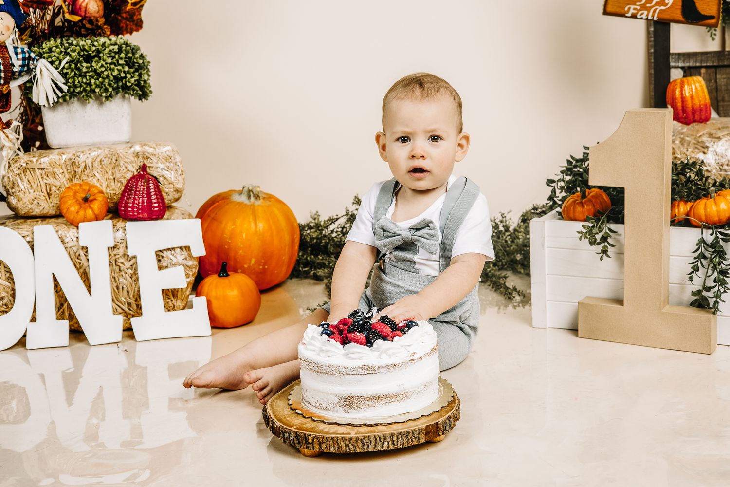 boy posing for his 1st birthday cake smash photoshoot during fall time